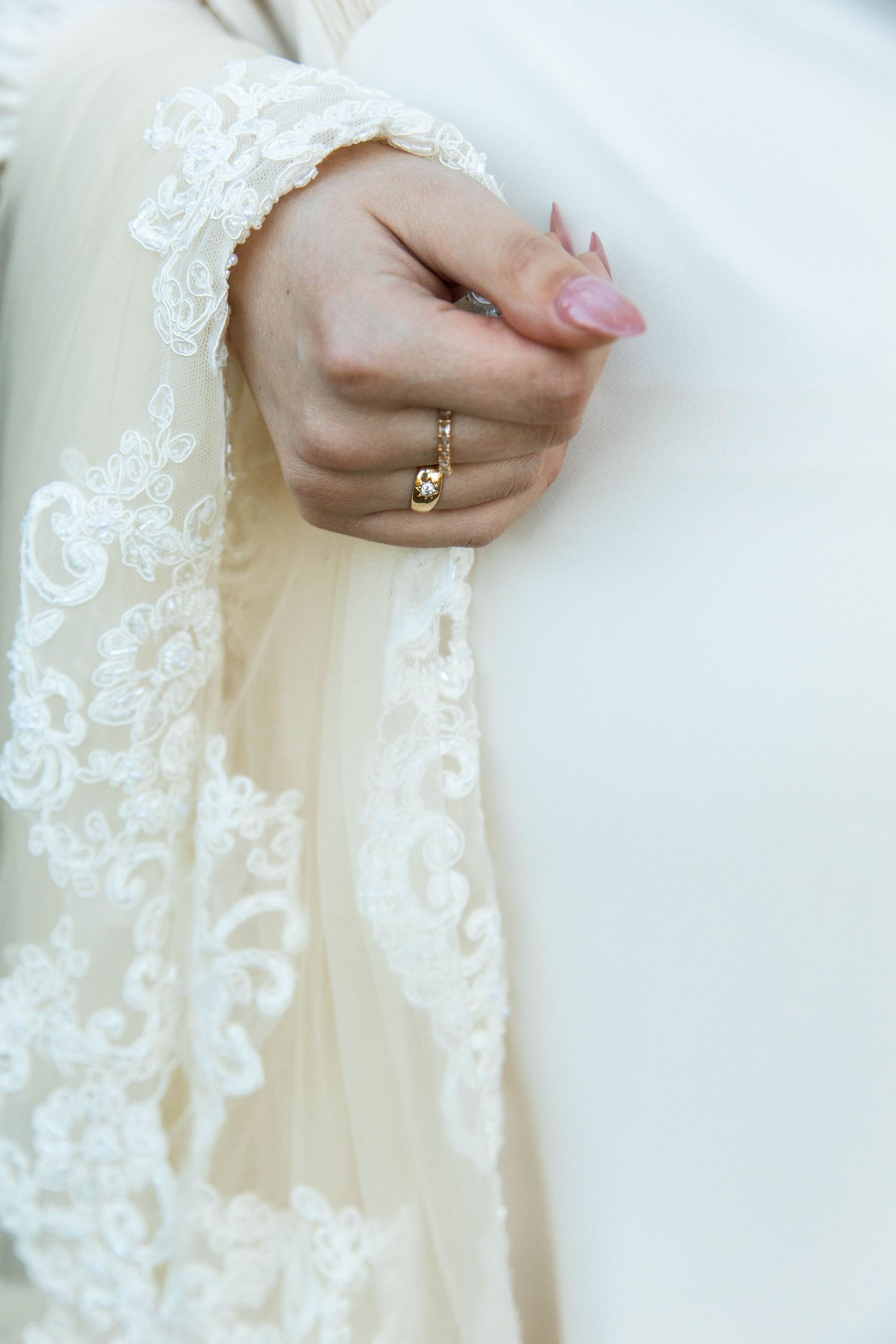 Close-up detail of a wedding dress with delicate lace trim and an engagement ring on a hand.