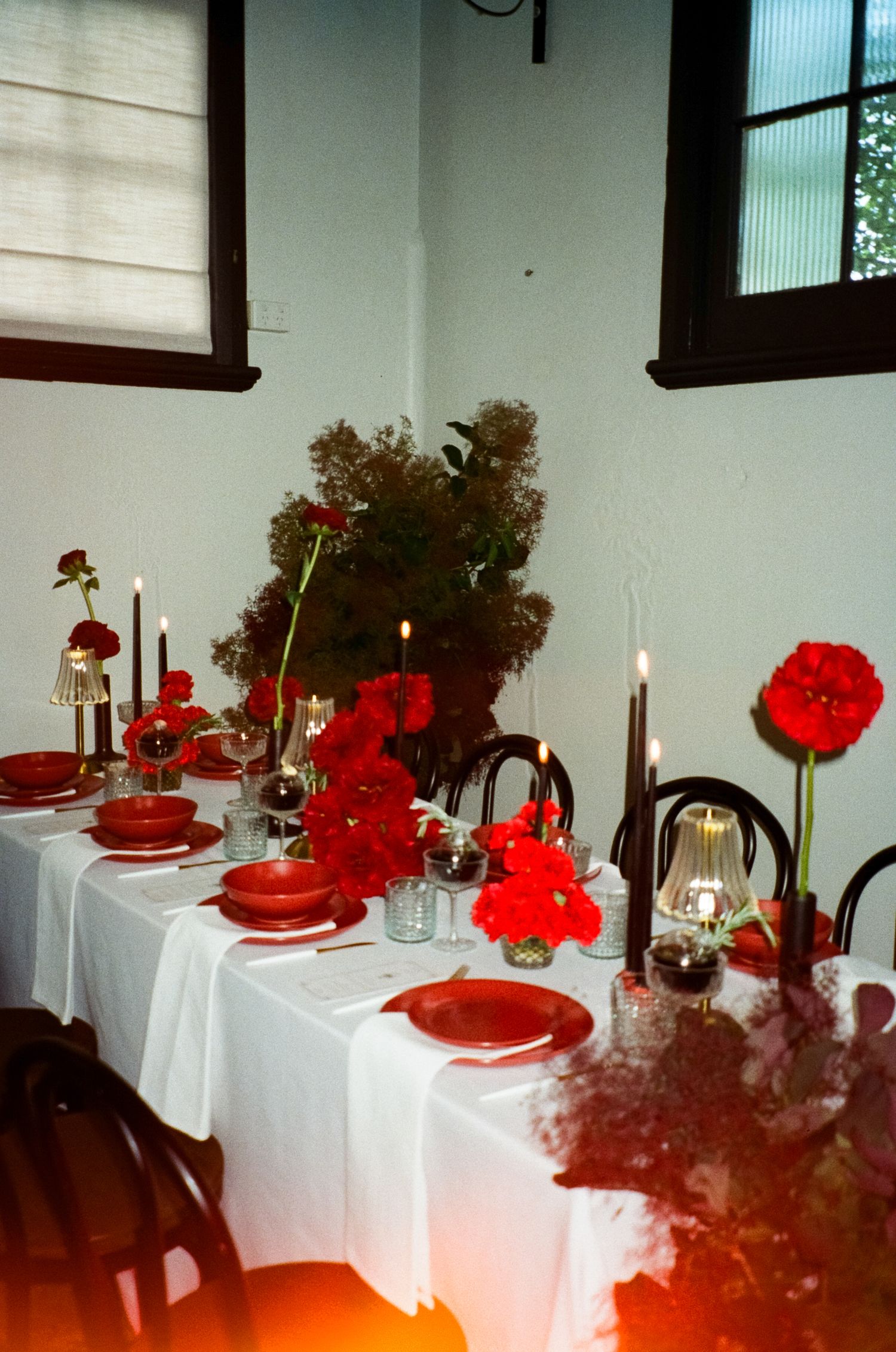 An elegant table setting with bright red carnations and white linens for a formal dinner event.