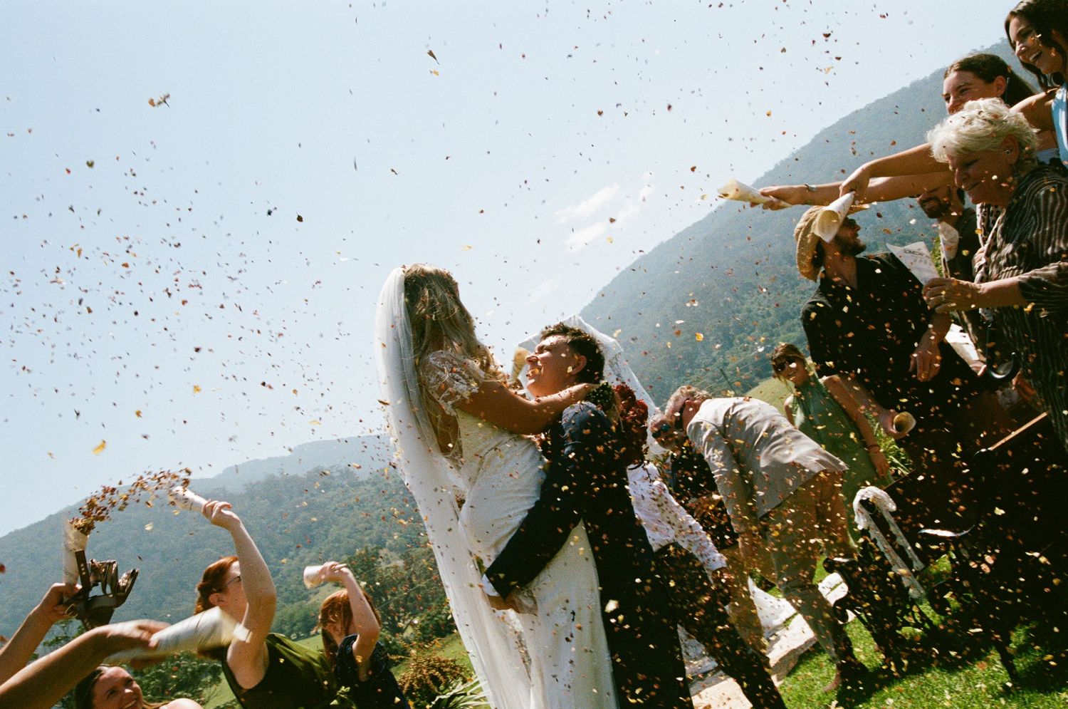 Wedding celebration with confetti being thrown in the air against a mountain backdrop.