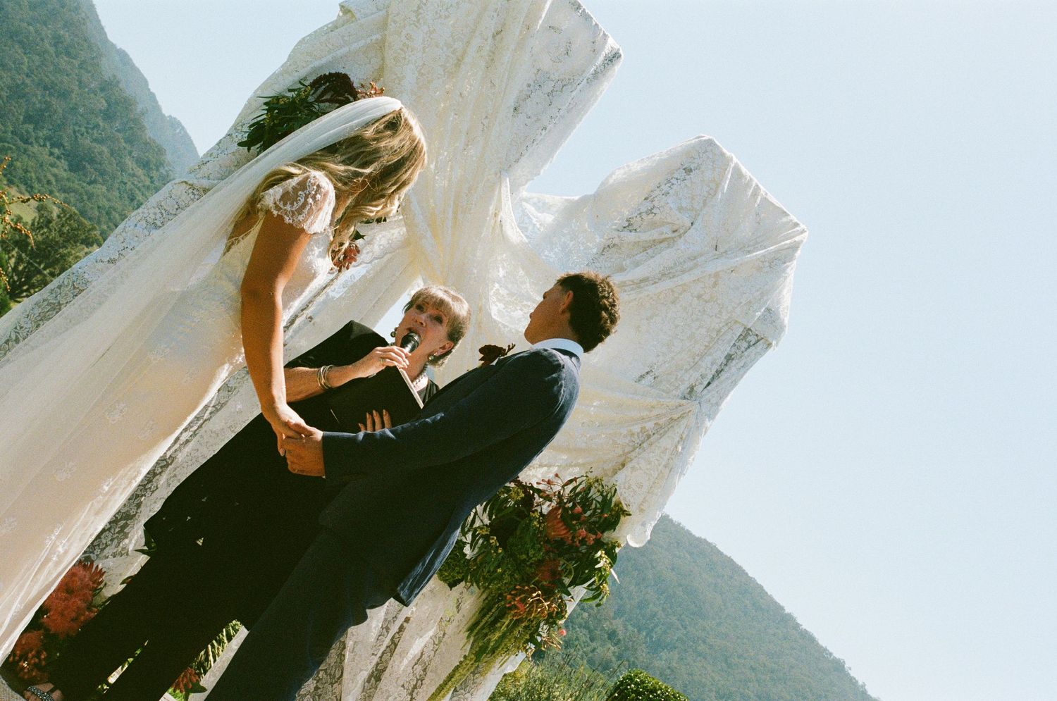 Wedding ceremony outdoors with guests gathered on a hillside overlooking mountain vistas.