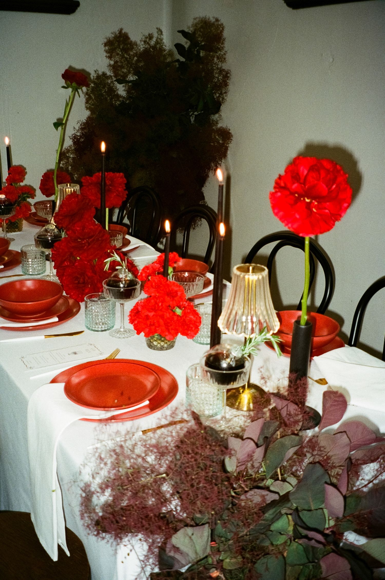 An elegant wedding table setting with bright red carnations and white linens for a romantic dinner celebration.