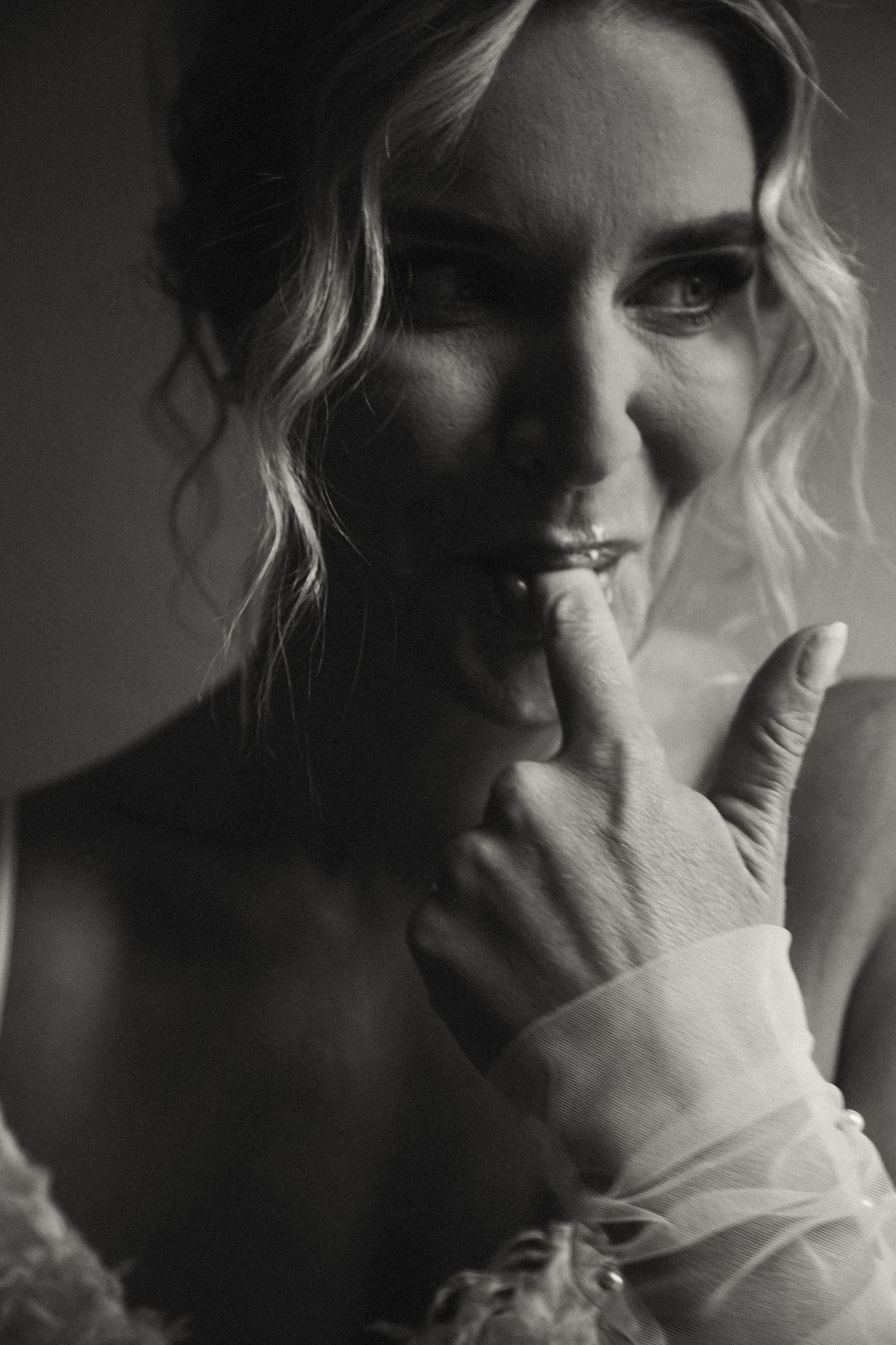 Dramatic black and white portrait of a person with wavy hair touching their mouth in an intimate artistic pose.