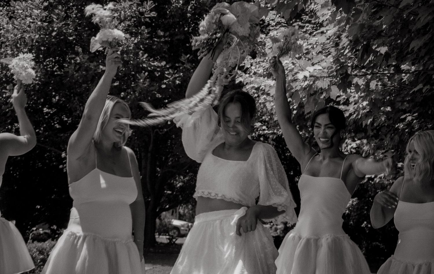 People in white dresses dancing joyfully outdoors during a celebration in black and white photography.