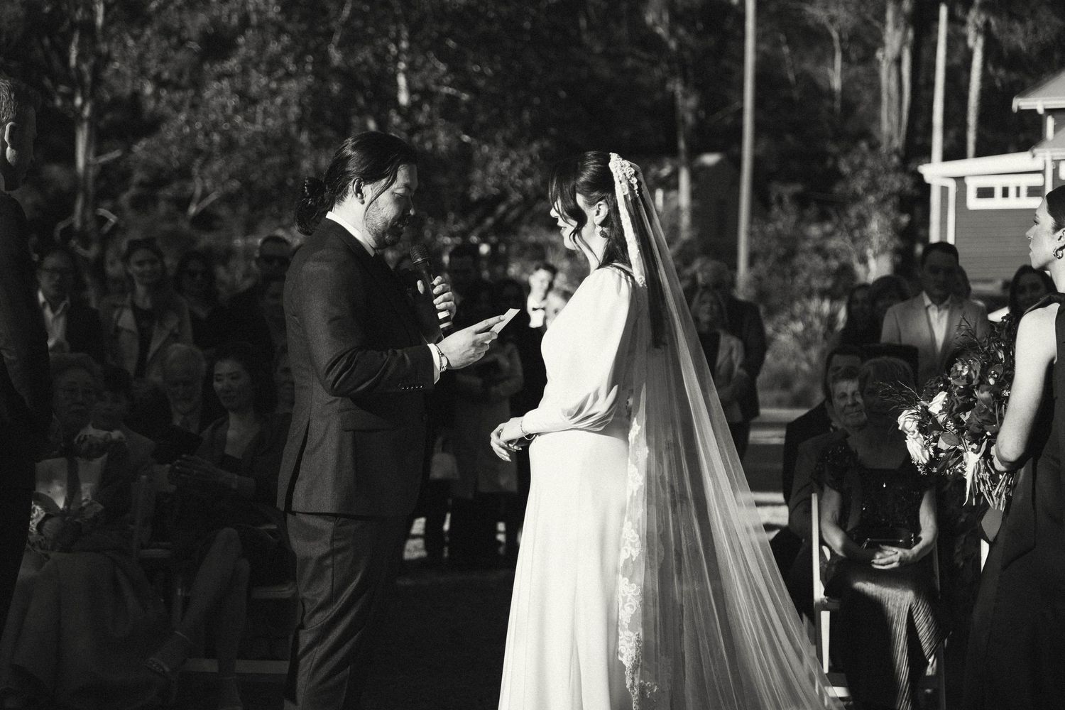 A couple exchanges vows during their outdoor wedding ceremony as guests watch.