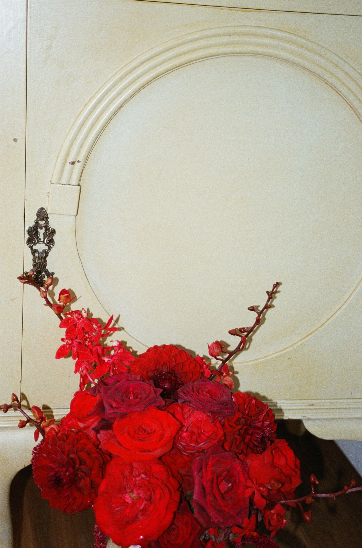 Vibrant red roses and floral arrangements against a white architectural wall with curved molding.