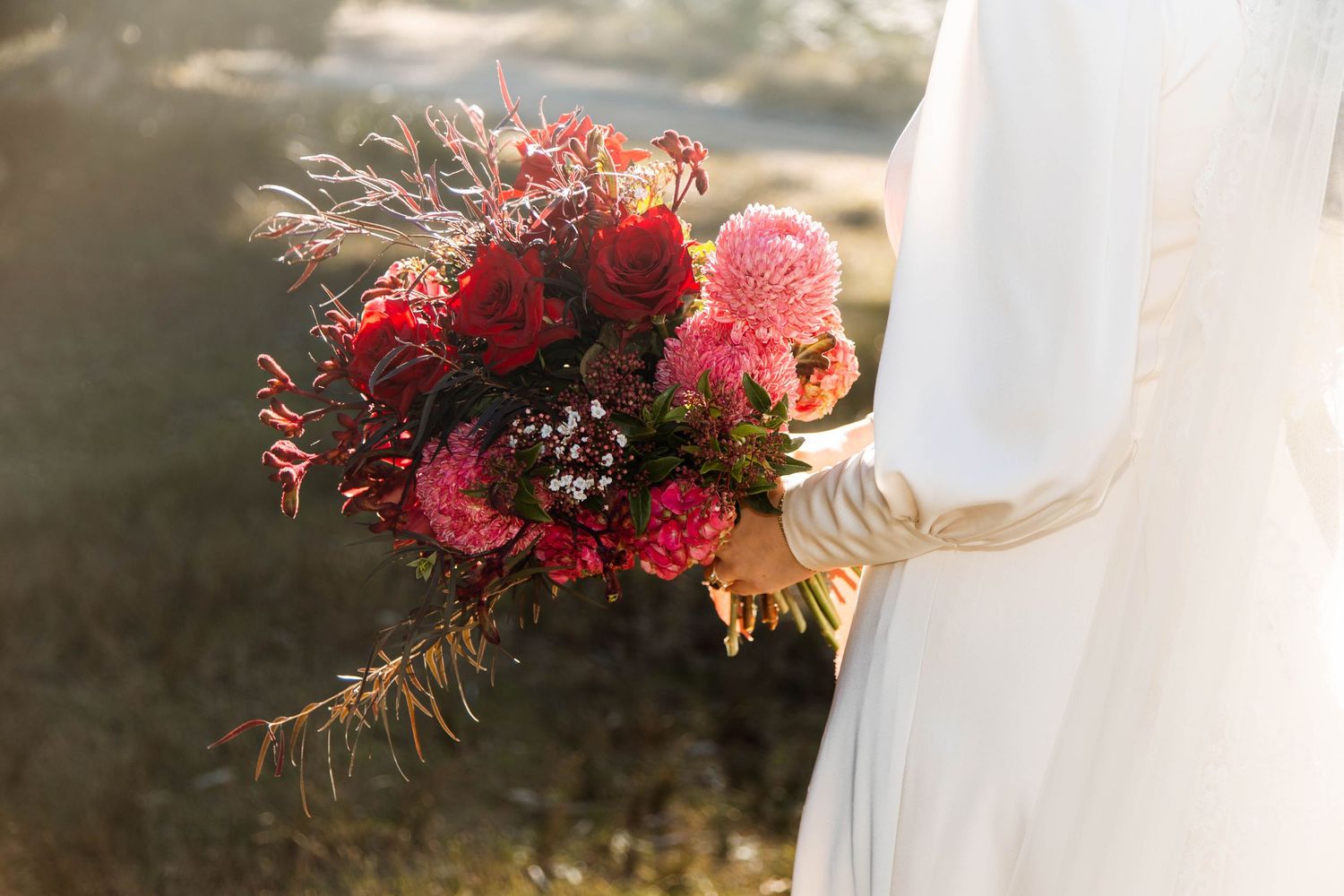 Close-up view of a colorful pink and red floral bouquet in natural sunlight against a blurred background.