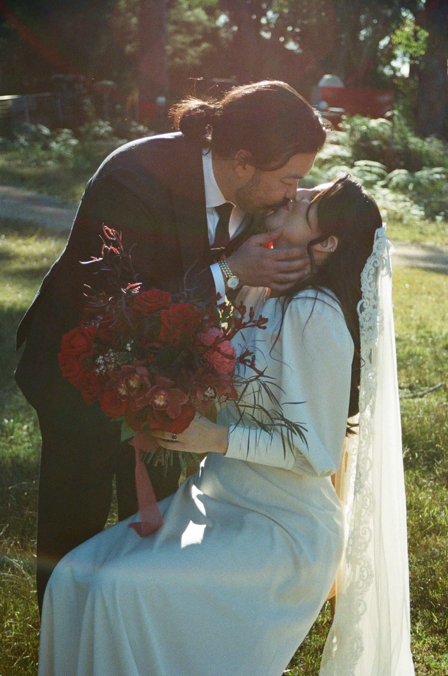 A romantic wedding scene in a sunlit garden with red roses.