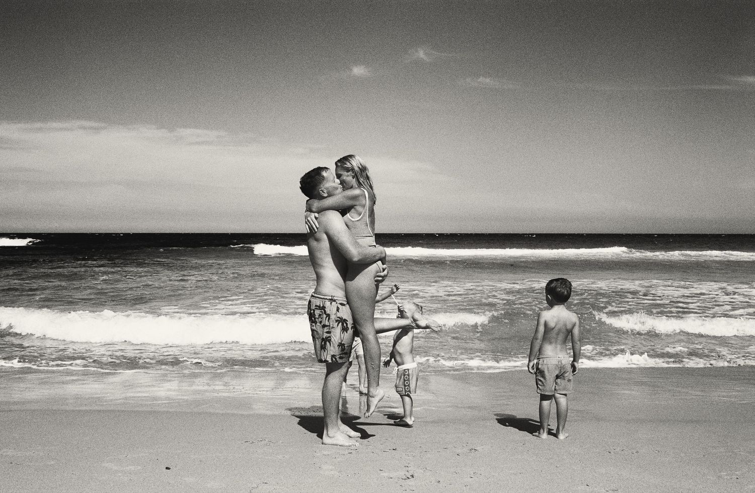 Black and white beach scene with family silhouettes against ocean horizon.