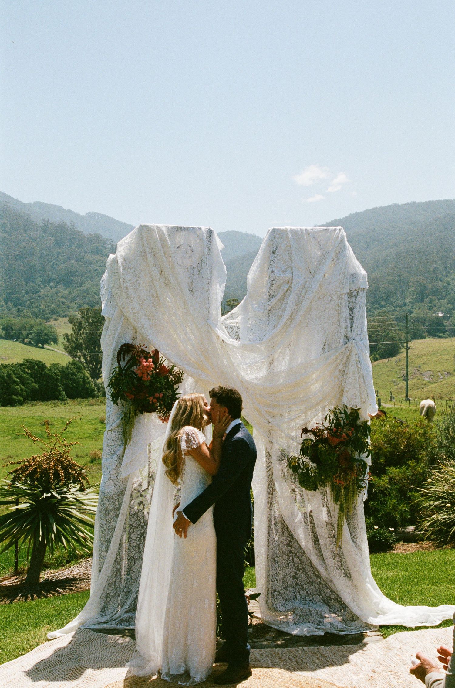 Wedding dresses displayed outdoors against a mountain backdrop with white lace details.