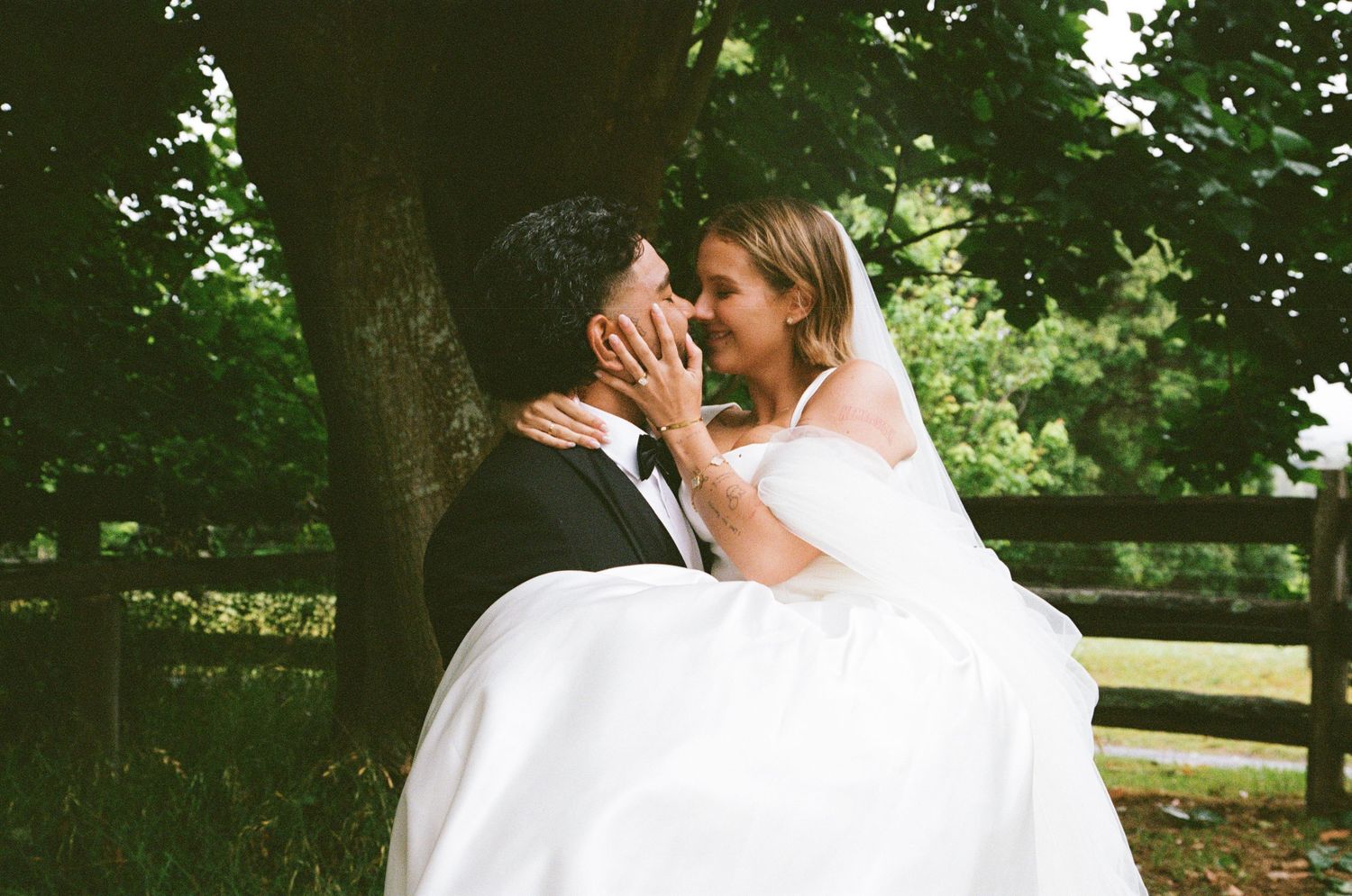 Romantic wedding couple shares intimate moments in lush garden setting with wooden fence.