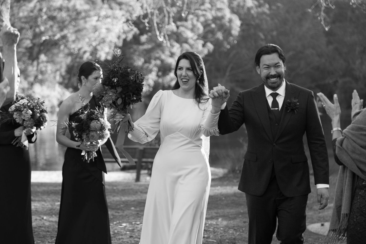 Wedding couple joyfully walks down the aisle together at outdoor ceremony while guests celebrate.