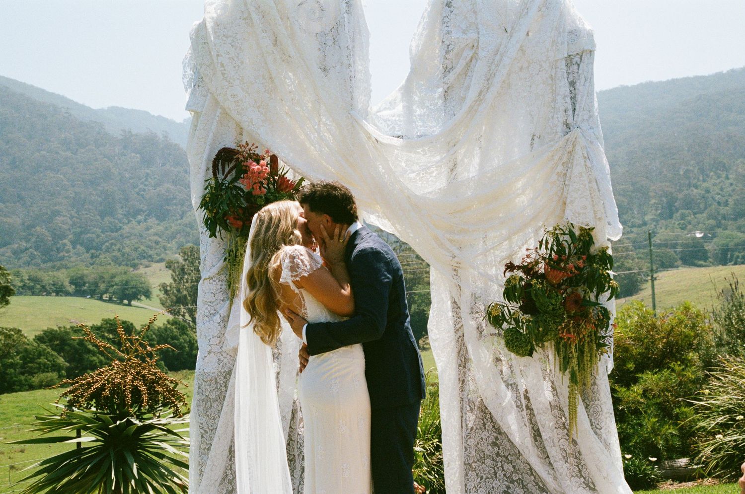 Elegant white lace wedding arch setup with mountain views in background.