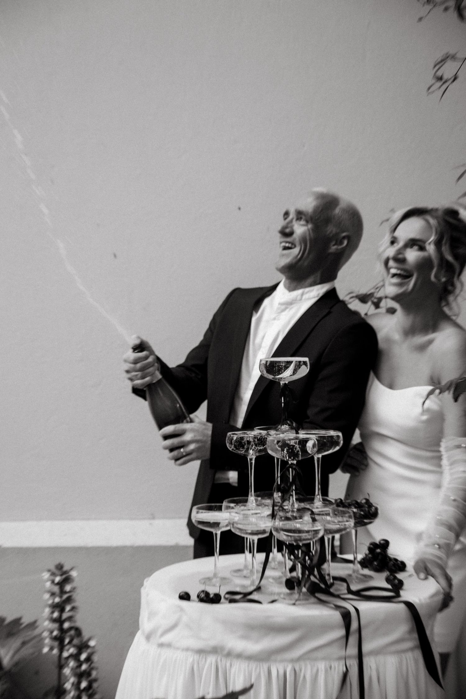 Wedding celebration with champagne tower and joyful couple popping bottles.