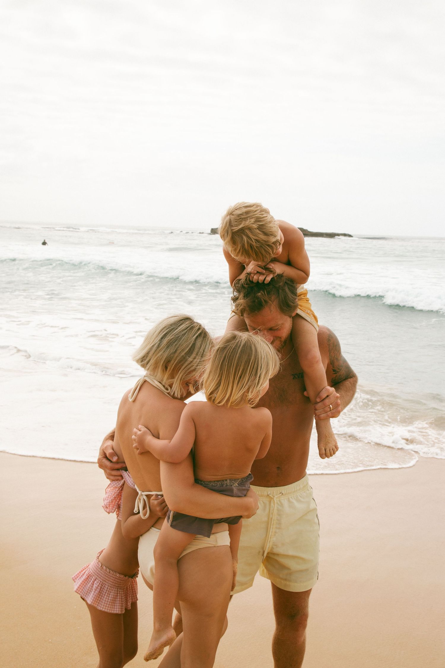 Family enjoying a sunny day together at the beach with waves crashing in the background.