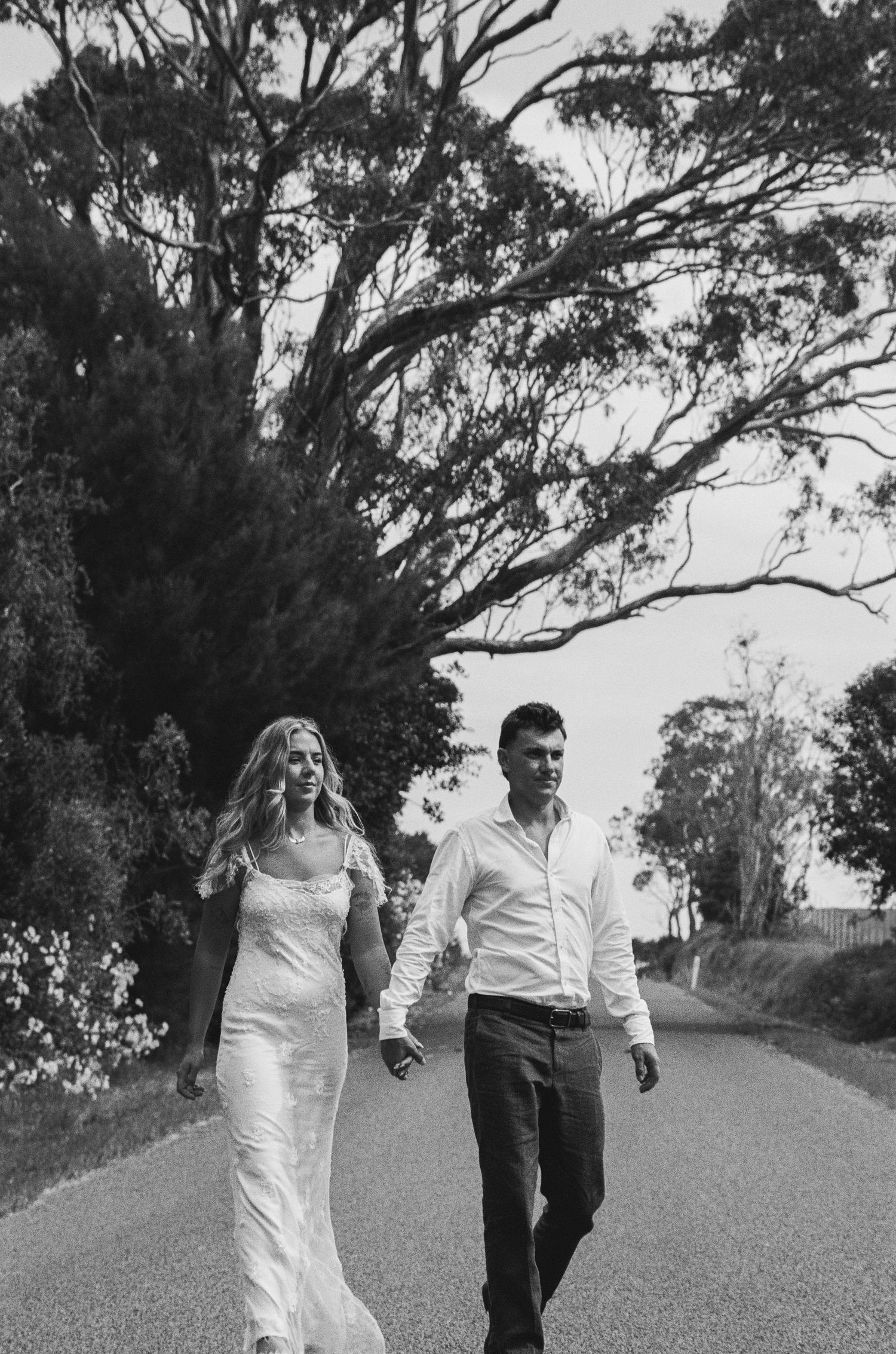 A couple walks along a tree-lined path in black and white photography.