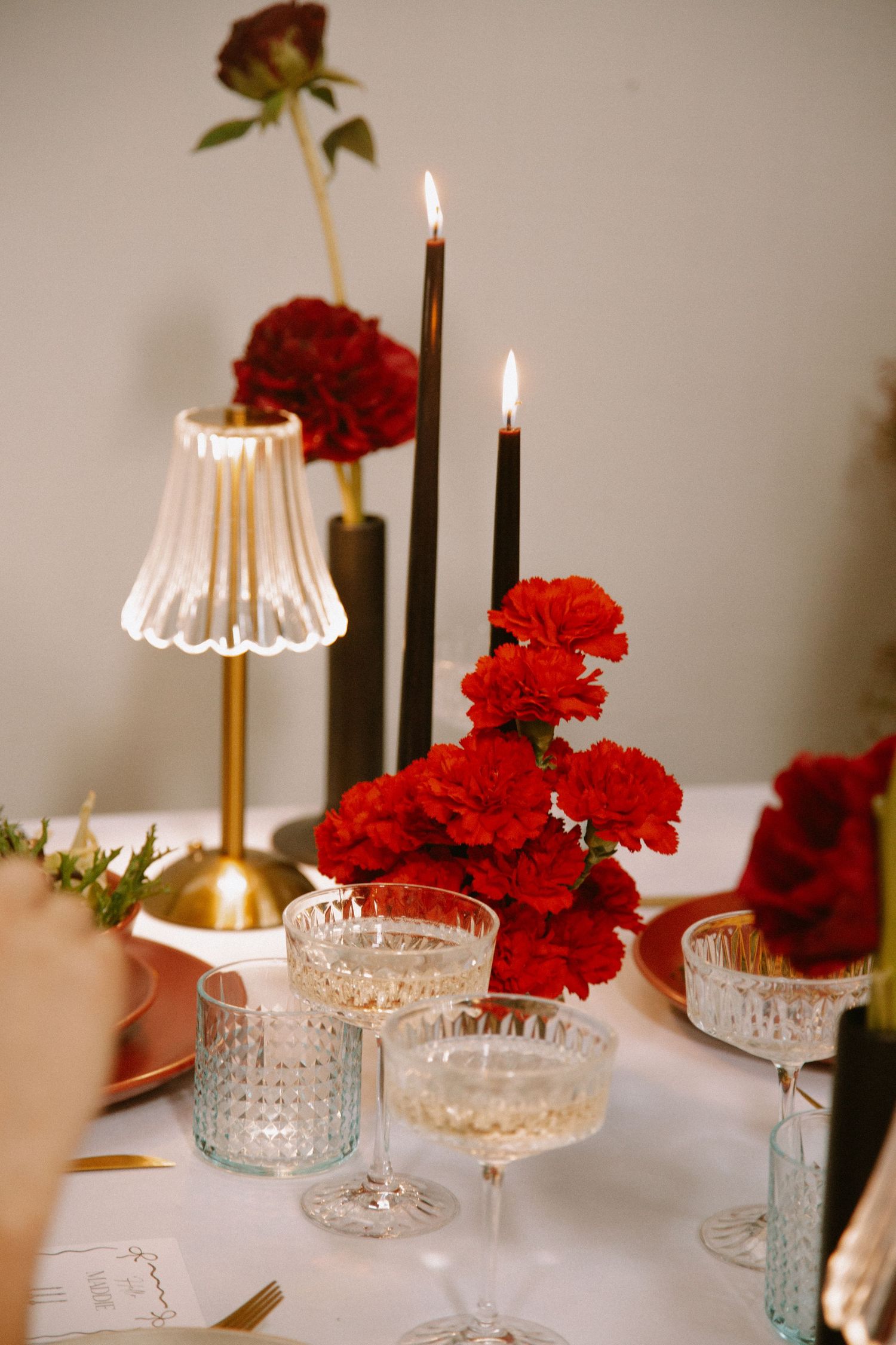 Intimate table setting with crystal glassware, lit candles, and deep red carnation arrangements.