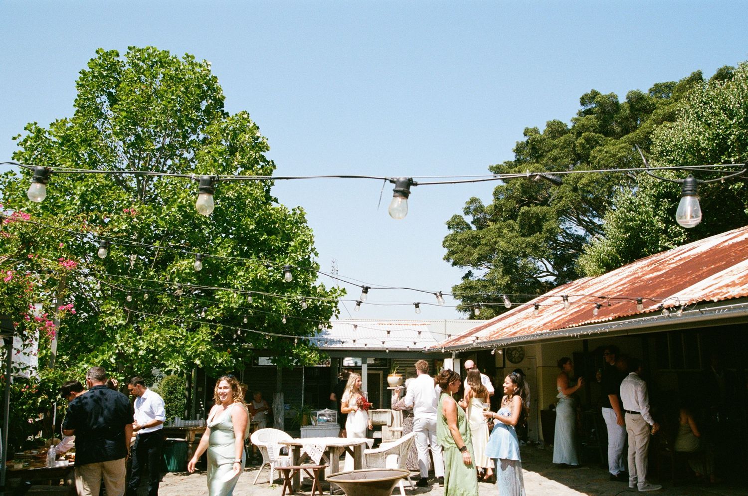 People dancing outdoors at a festive summer party with string lights and rustic buildings in the background.