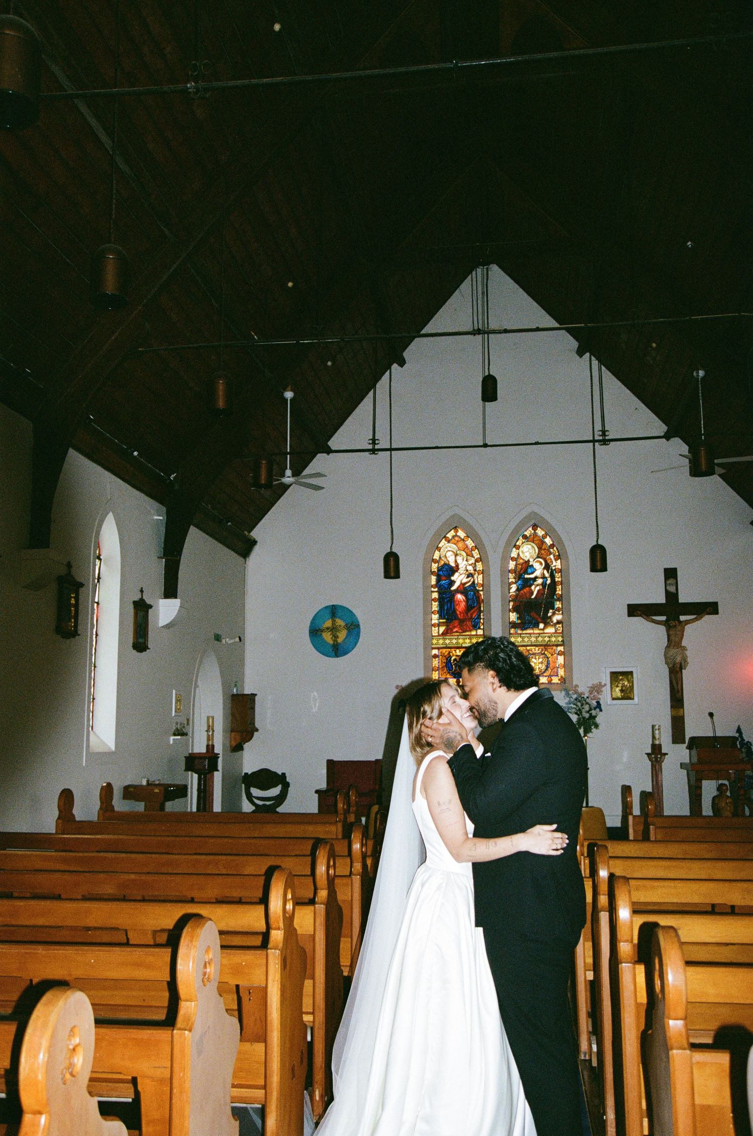A couple shares their first kiss as newlyweds in a traditional church with stained glass windows and wooden pews.