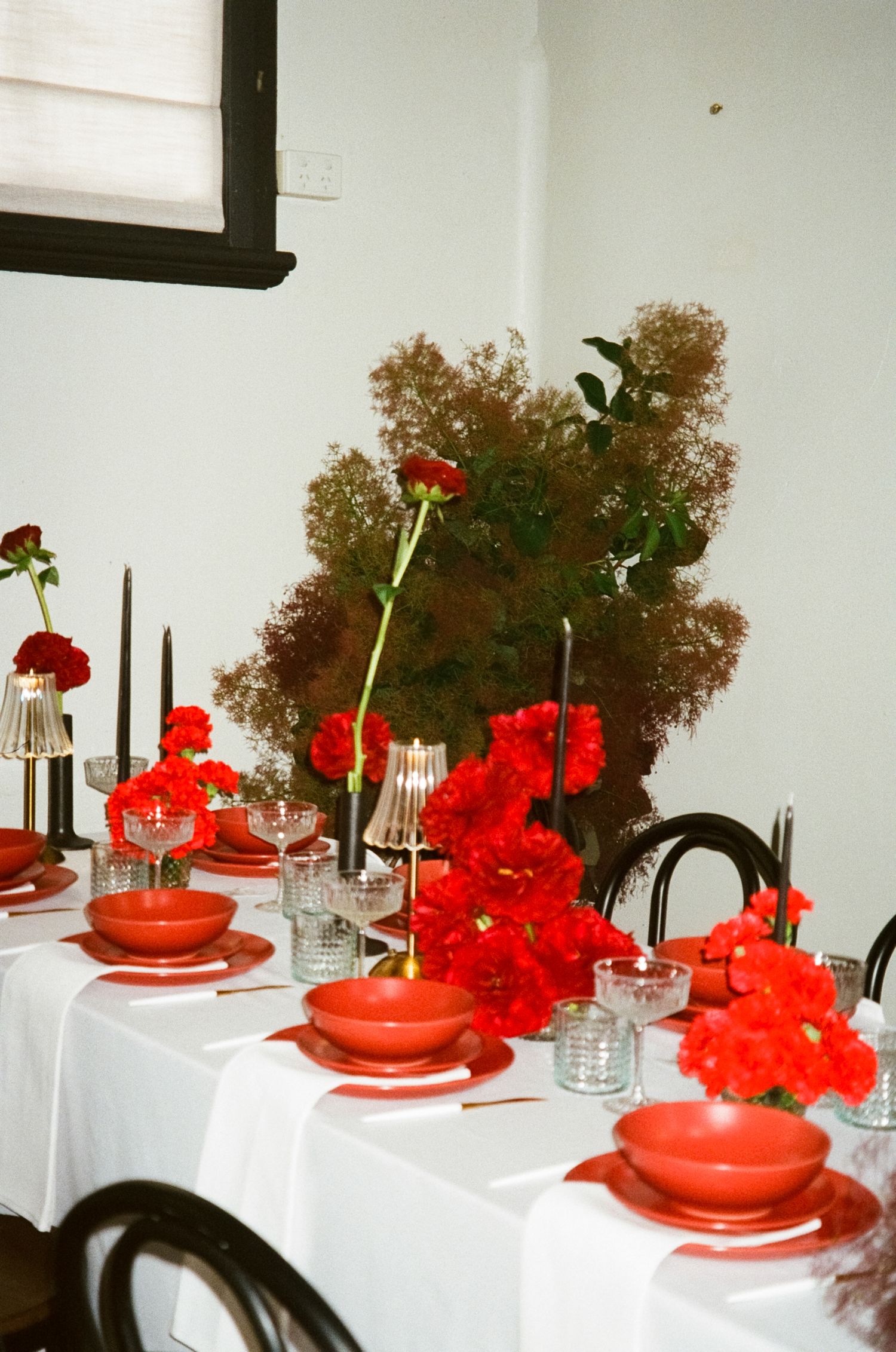 Elegant table setting with bright red flowers and place settings arranged on white tablecloths for a special occasion.