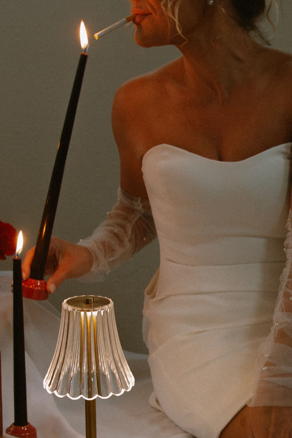 Someone in a white dress lights a candle in a translucent glass holder creating a warm atmospheric glow.
