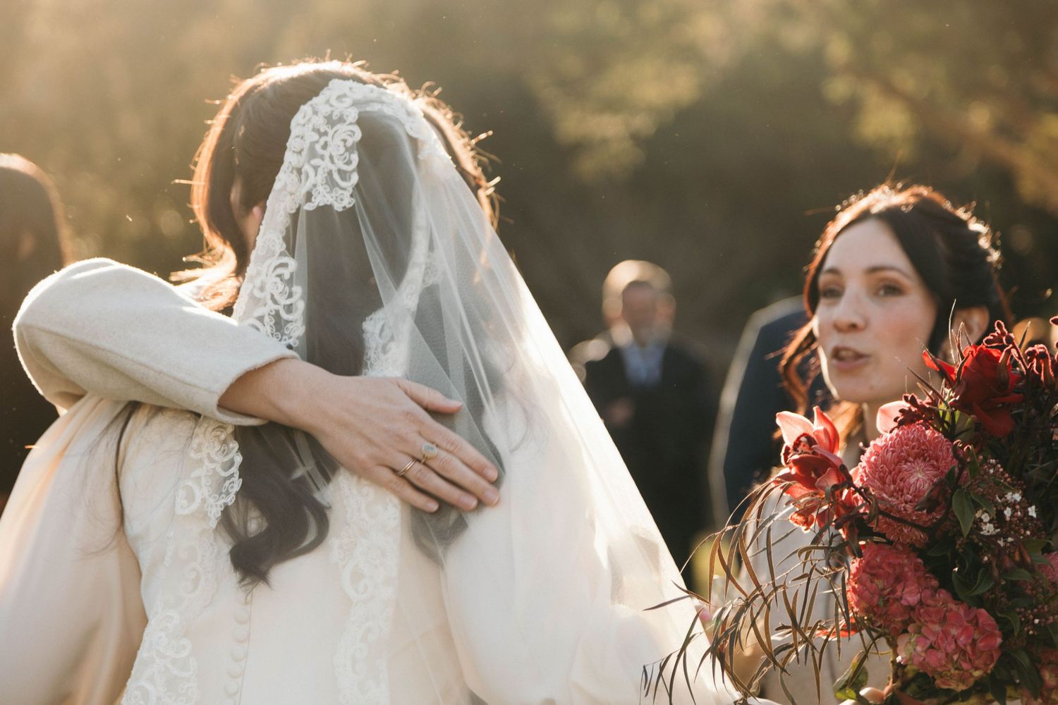 Golden sunlight illuminates wedding party members gathered outdoors with burgundy floral bouquets.