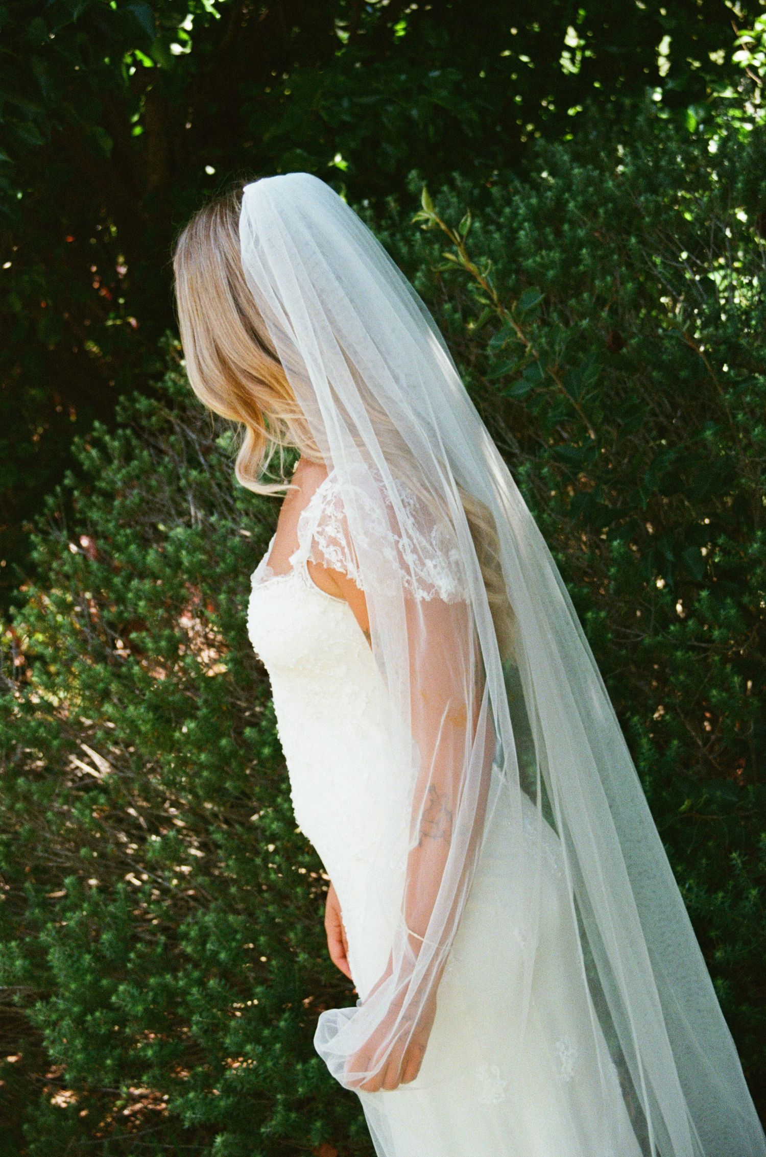 Elegant bridal veil and lace wedding dress details captured in a garden setting.