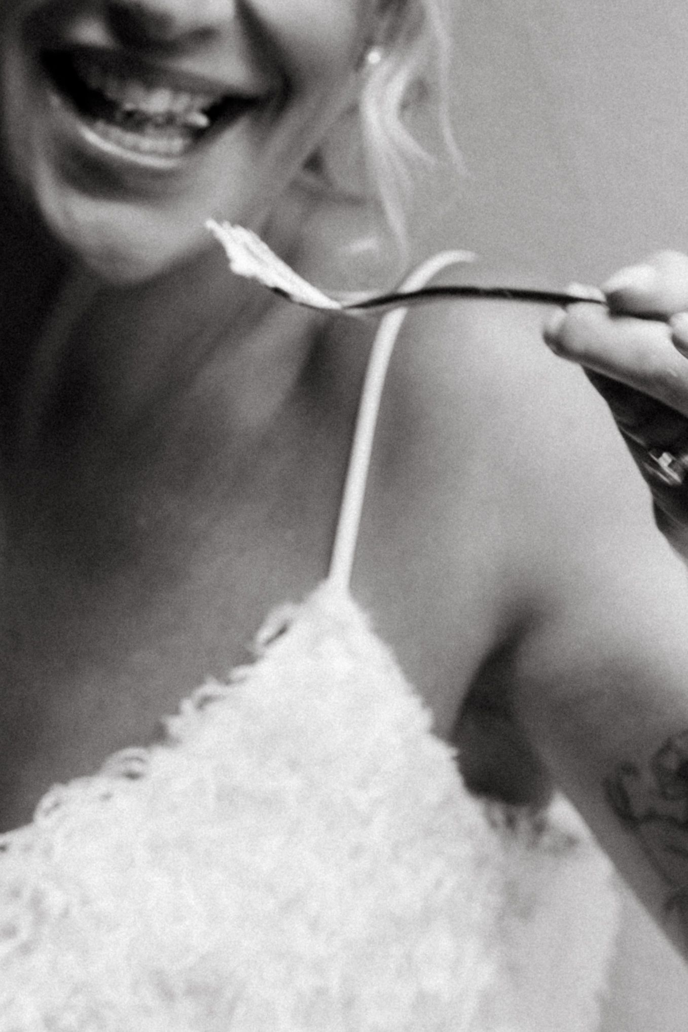 Black and white close-up image showing a bright smile and thin dress strap being adjusted against light fabric.
