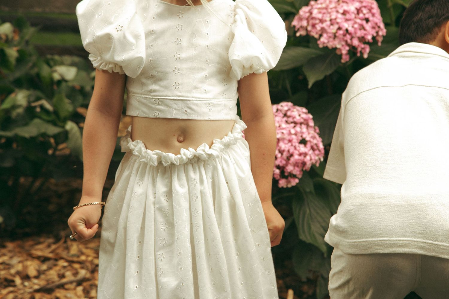 A cropped view of a two-piece white wedding dress with puff sleeves and pink hydrangeas in the background.