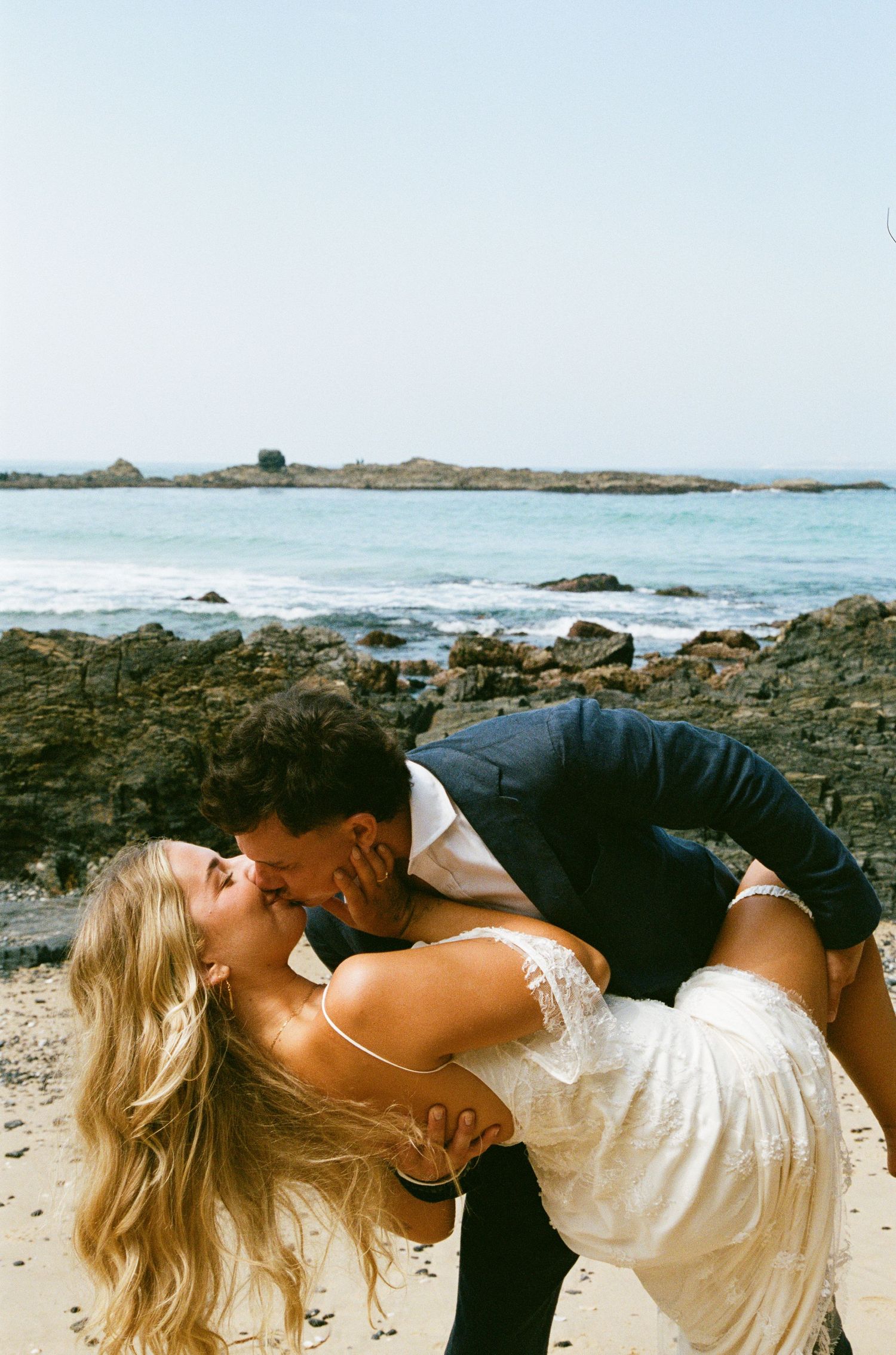A romantic moment captured on a scenic beach with volcanic rocks and crashing waves.