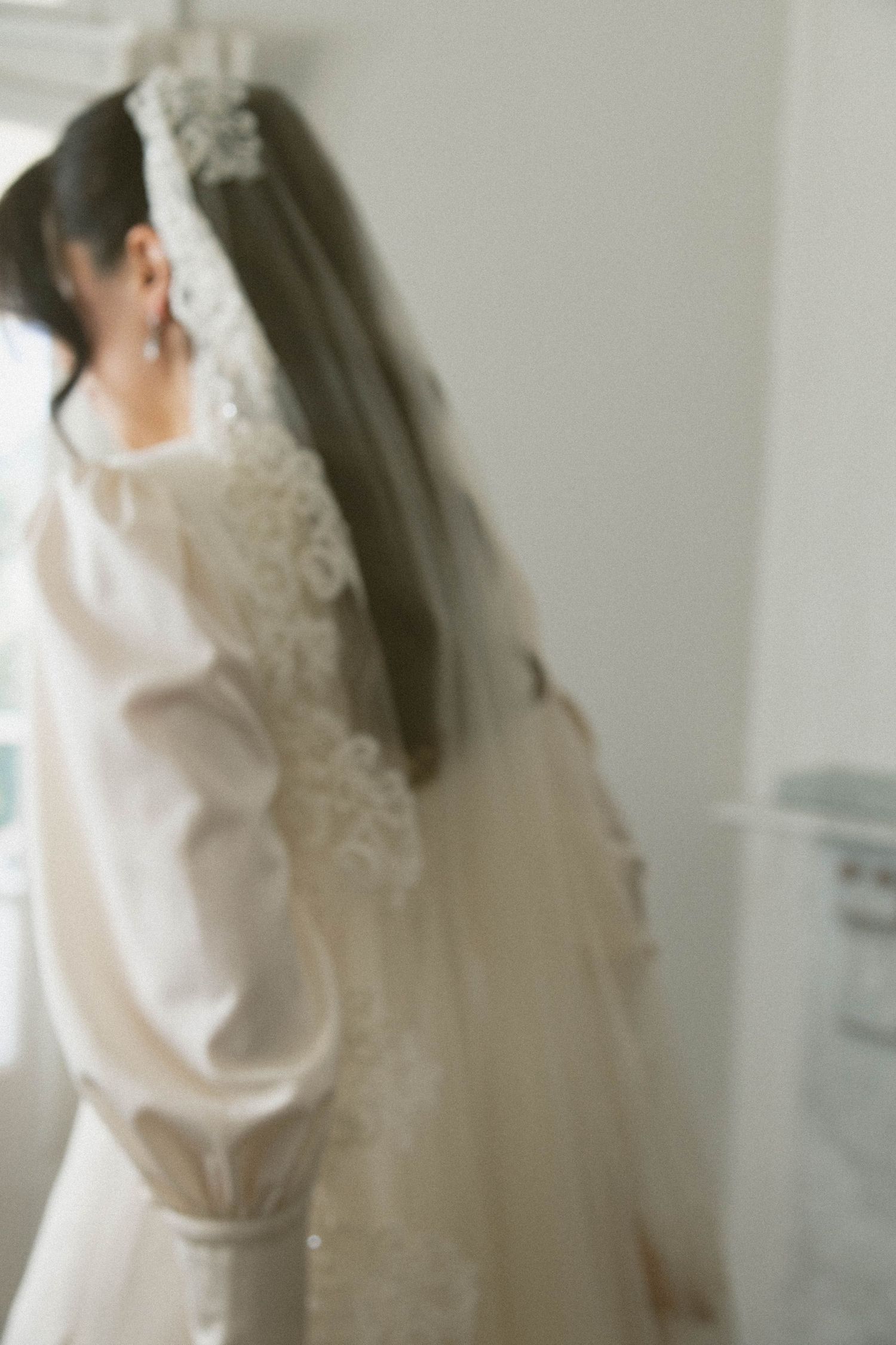 Bride in a classic white wedding gown adjusts her long flowing veil in an elegant getting ready moment.
