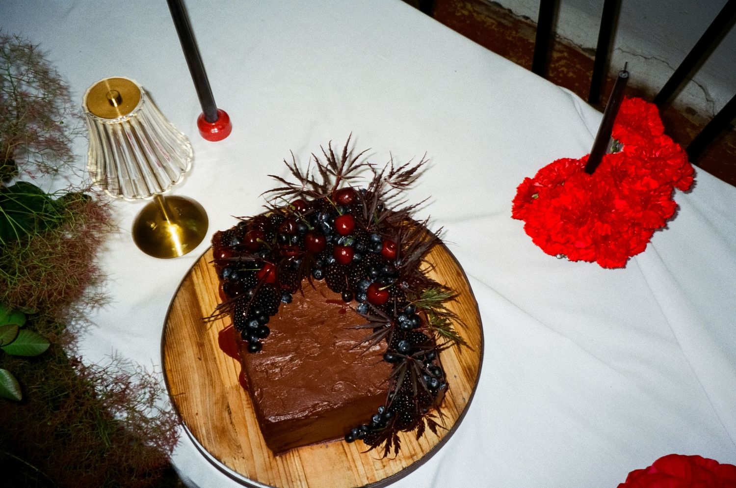 A chocolate cake with dark spiky decorations sits on a wooden plate next to a gold bell and red decorative items.
