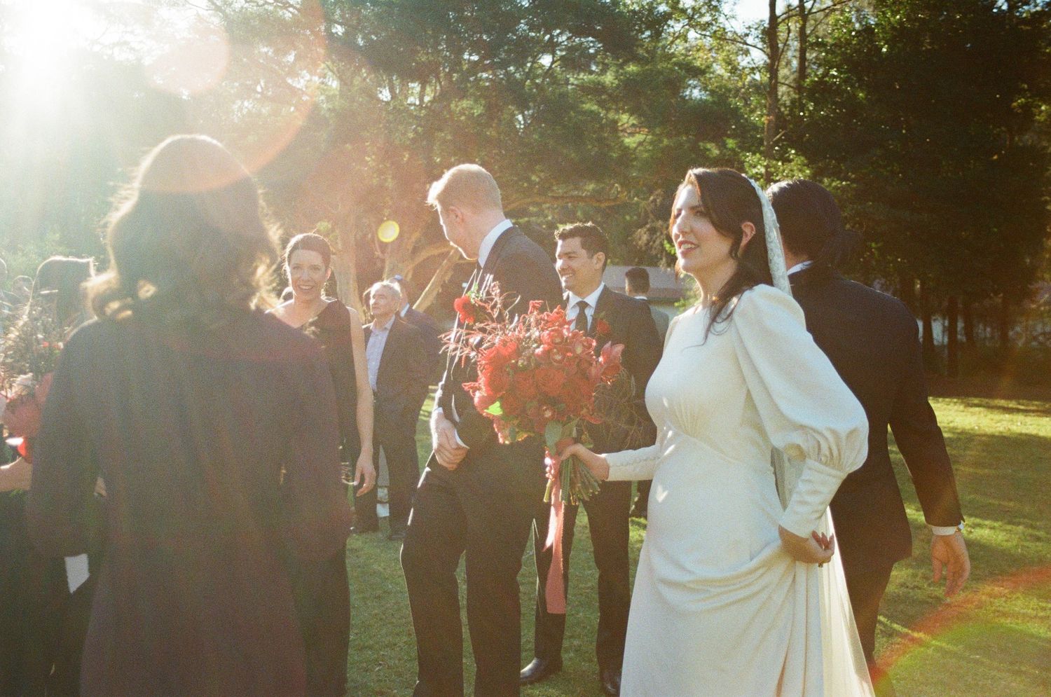 Wedding party members pose together in warm sunlight during golden hour at an outdoor ceremony.
