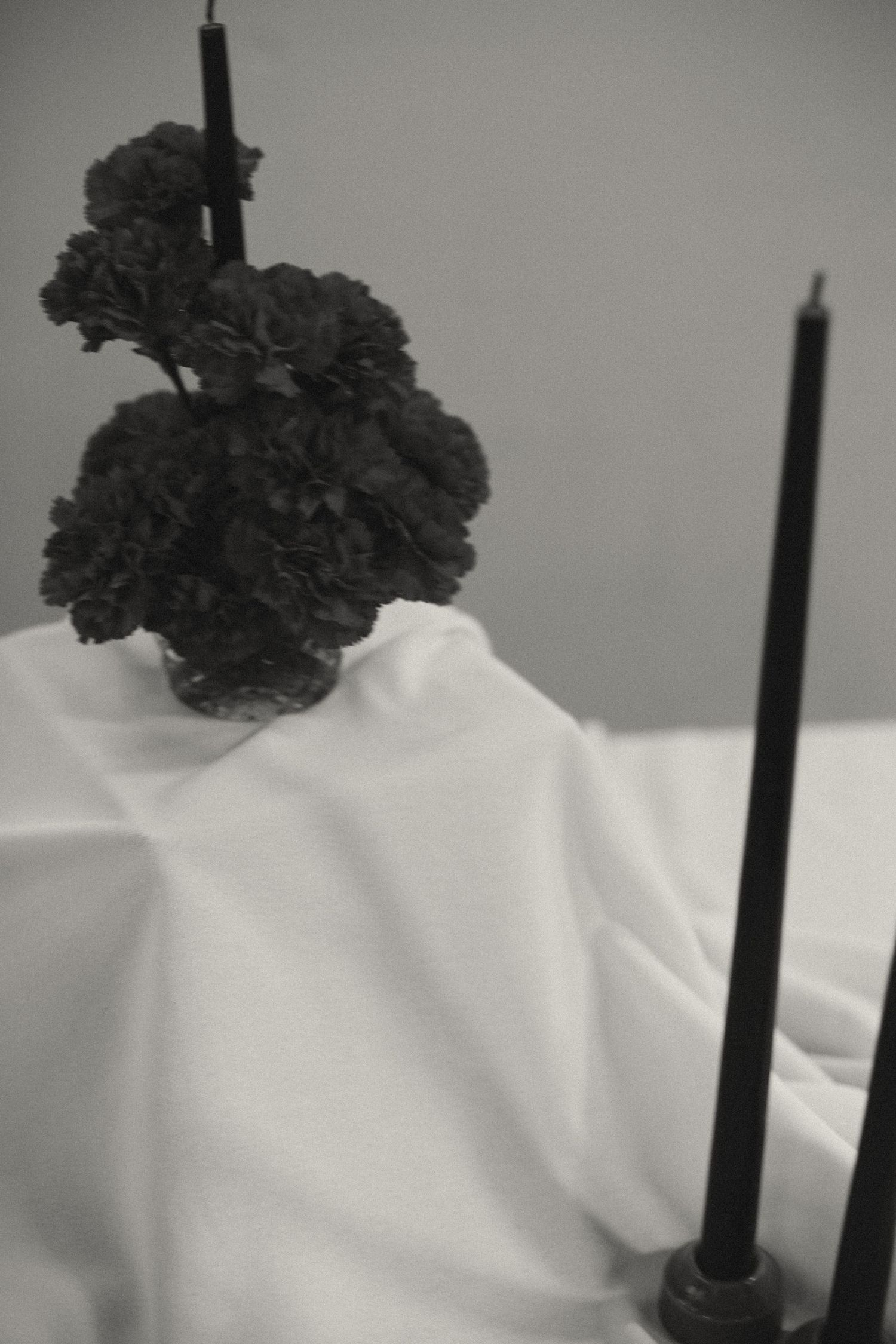 Dark carnations and tall black candles arranged on white tablecloth.
