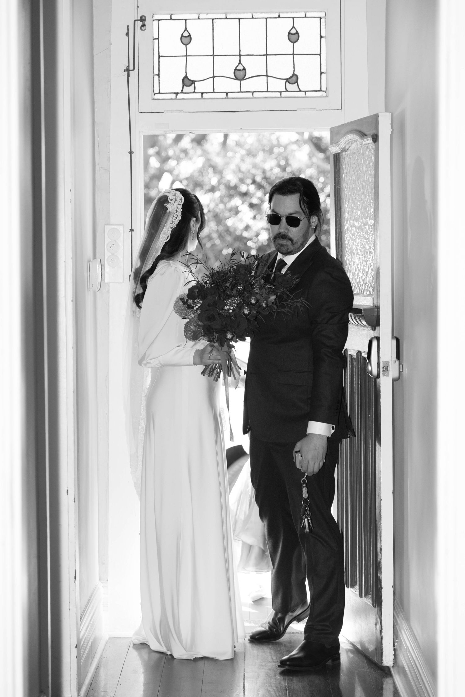 Black and white photo of newlyweds standing in doorway with decorative lighting fixture above.