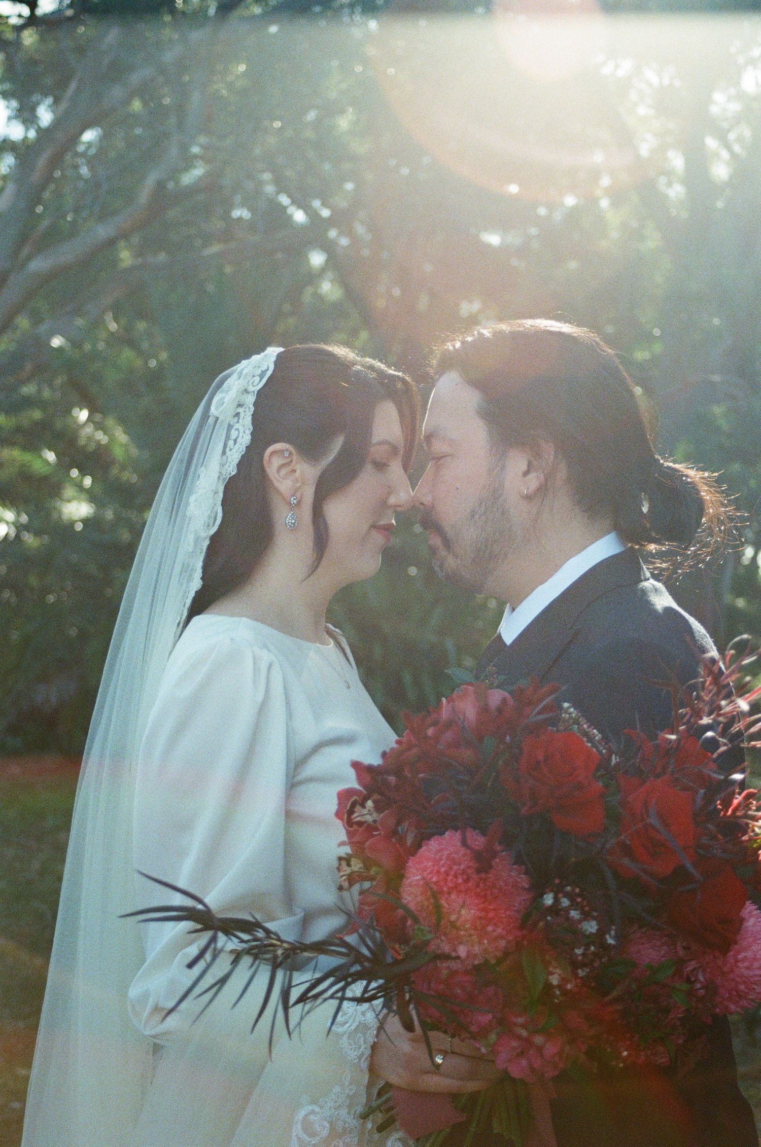 A romantic wedding photo with a dreamy sunlit effect, featuring a beautiful bouquet of red and pink flowers.