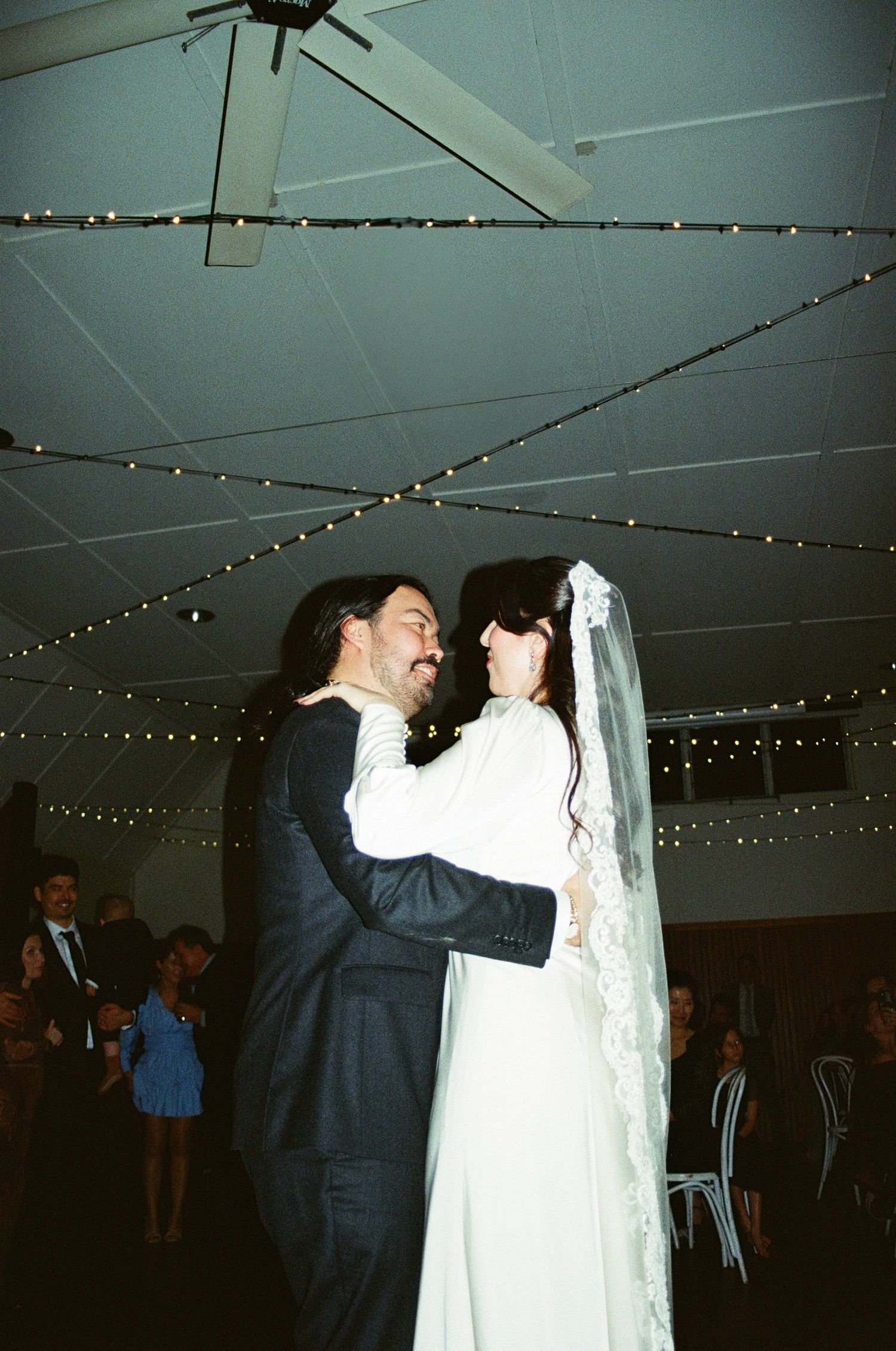 A couple shares their first dance at their wedding reception under strings of twinkling lights on the ceiling.