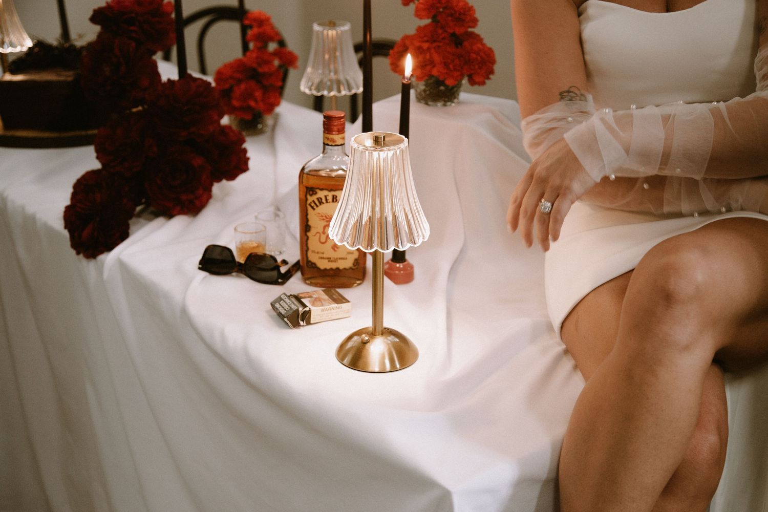 Elegant table setting with red flowers and vintage brass lamp against white linens.