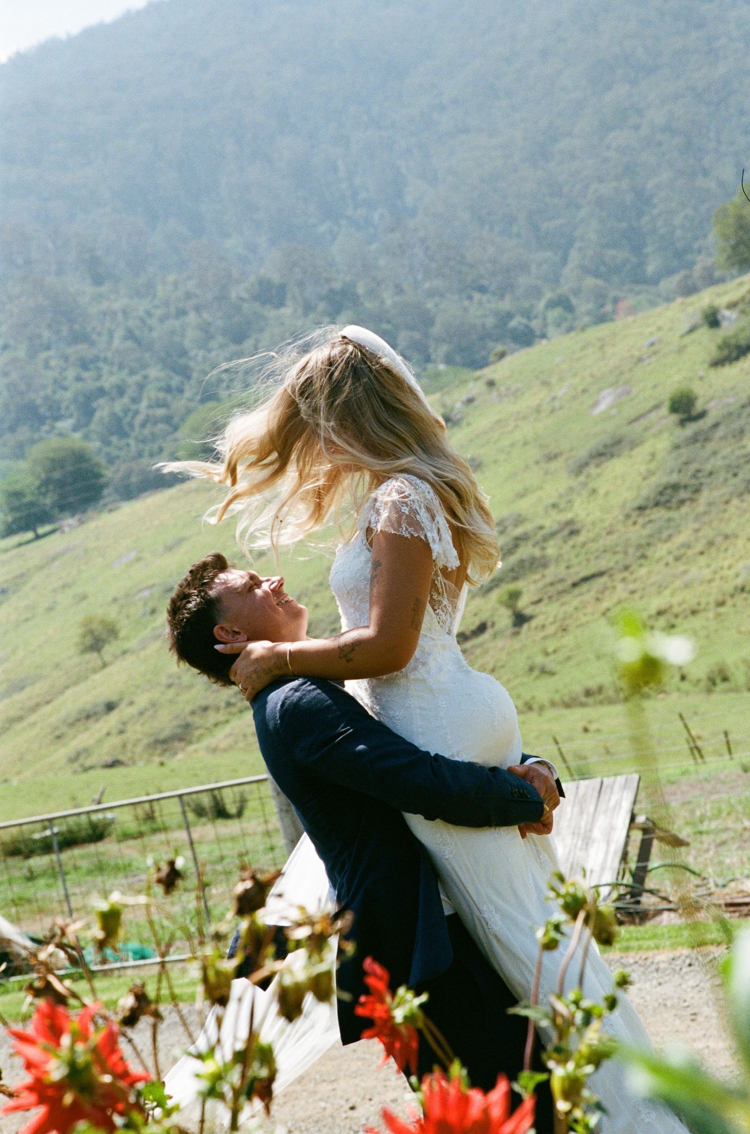 A romantic wedding scene unfolds against a mountainous backdrop with vibrant flowers.