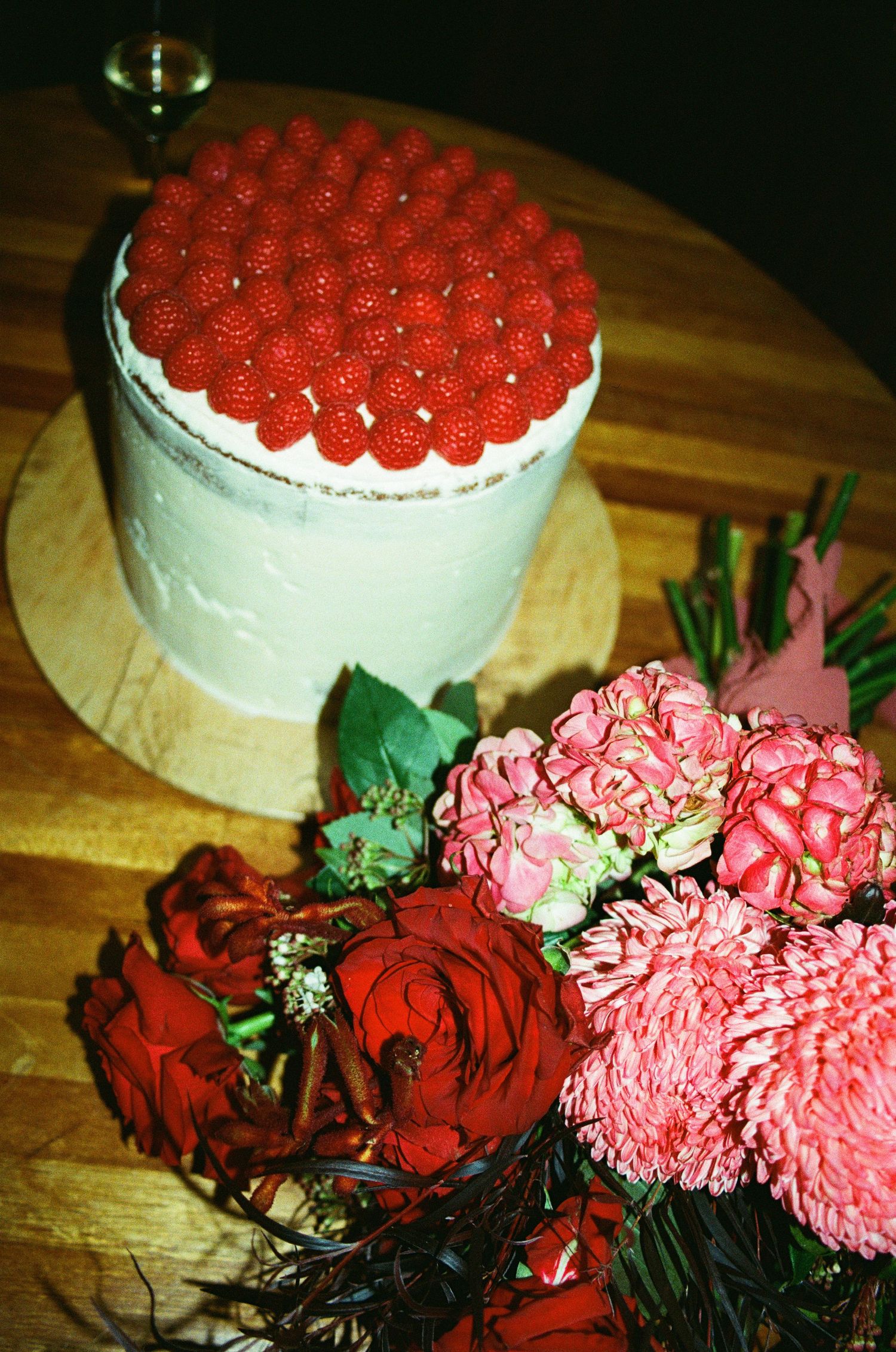 White wedding cake decorated with fresh red raspberries and pink and red roses.