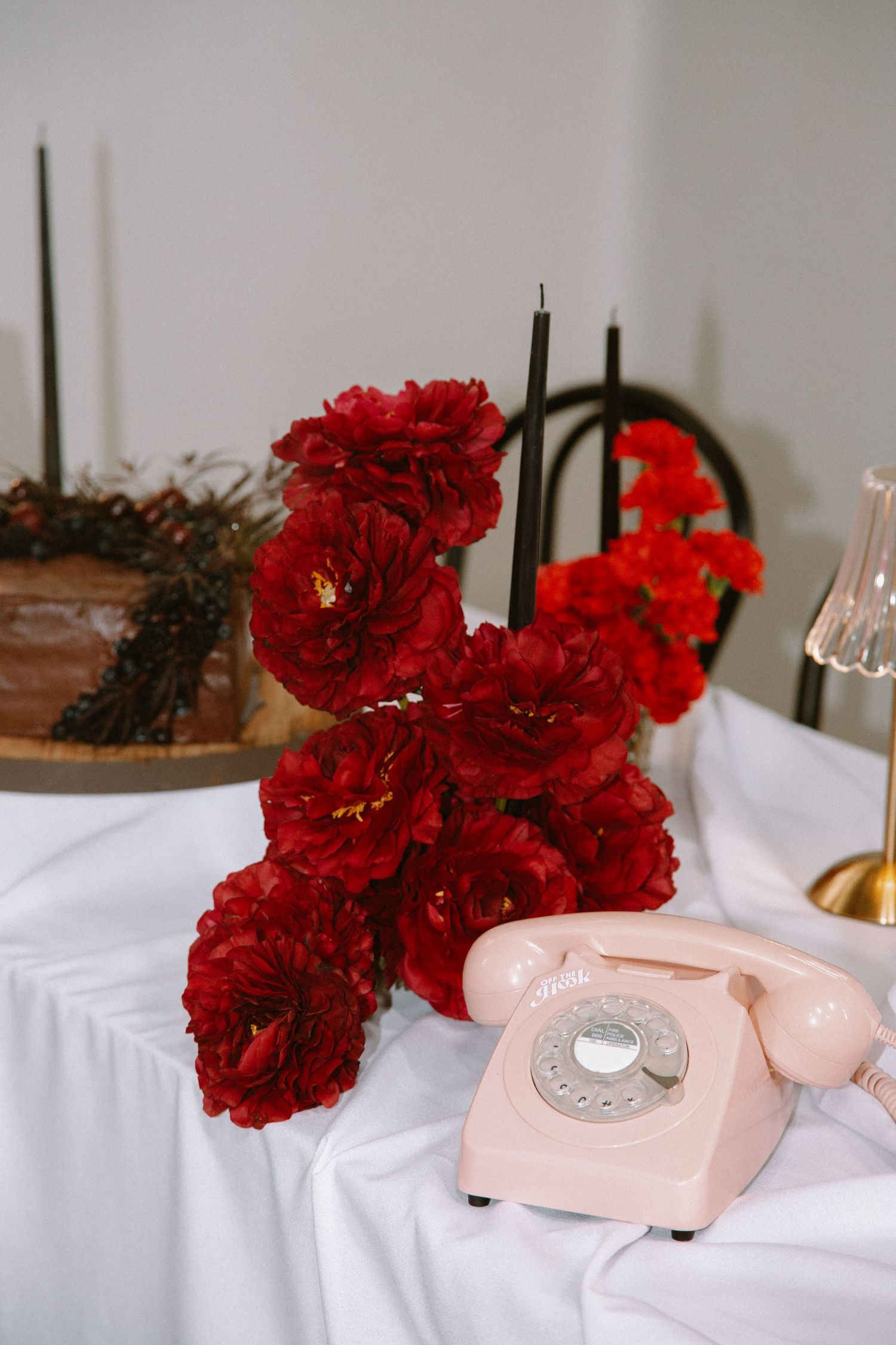 A vintage pink rotary telephone next to vibrant red roses on a white tablecloth.