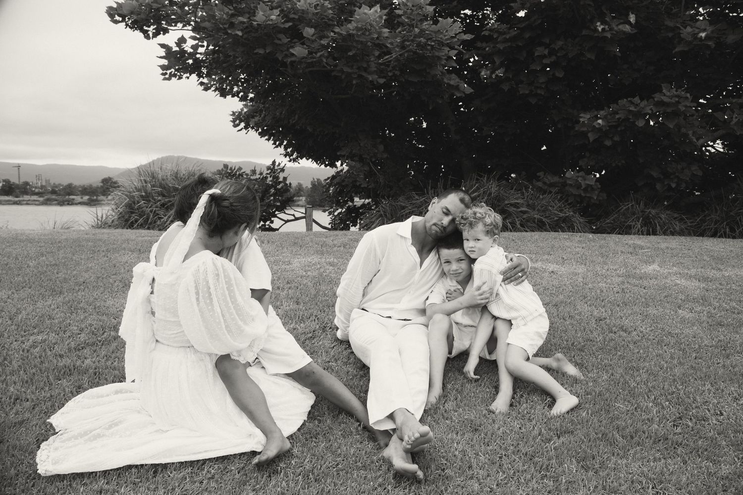 A black and white photograph of family members relaxing together on grass under a tree.