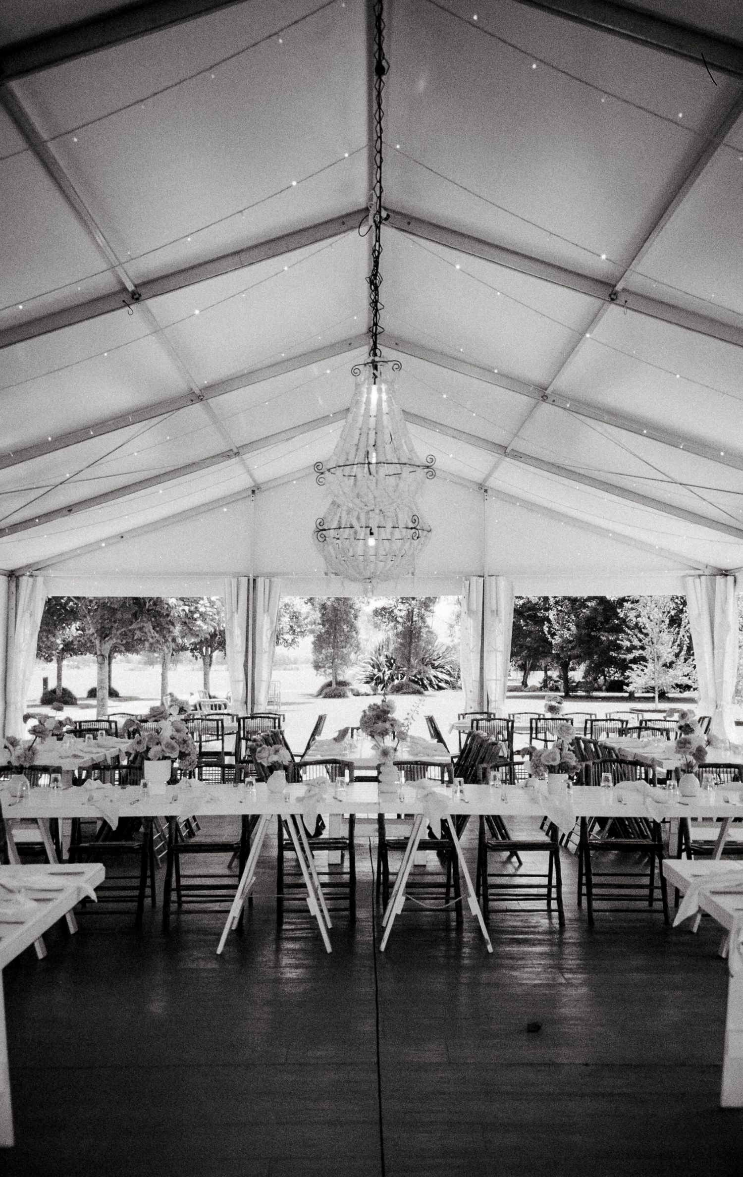 Black and white photo of an elegant reception tent interior with chandelier and table settings for a formal event.