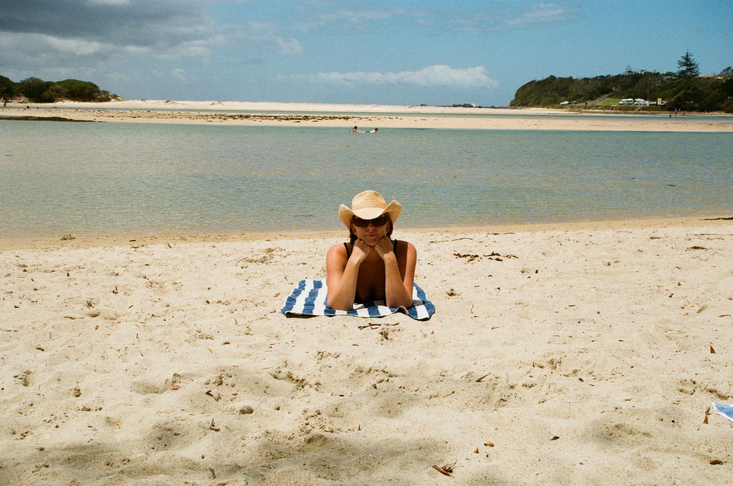 A ginger cat lounges on a white sandy beach with turquoise ocean waters and blue sky in the background.