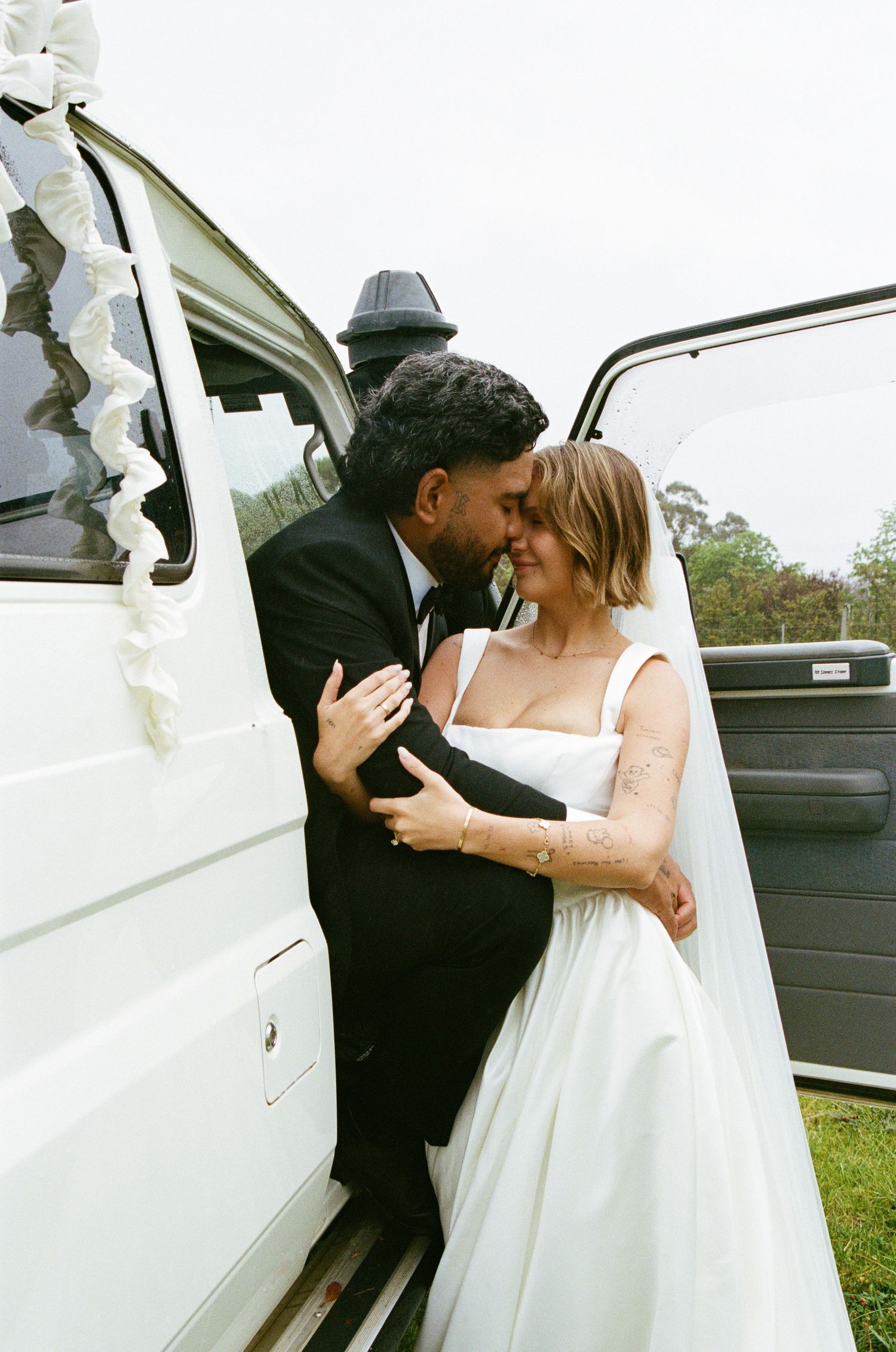 A romantic moment between a couple by a white car door during their wedding celebration.