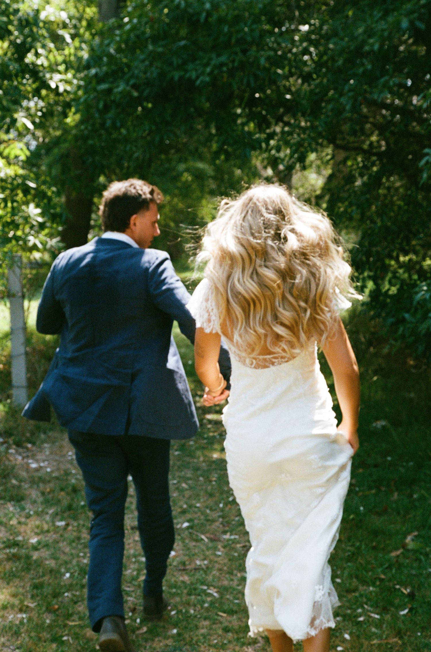 Newlyweds run playfully through a lush green garden setting.