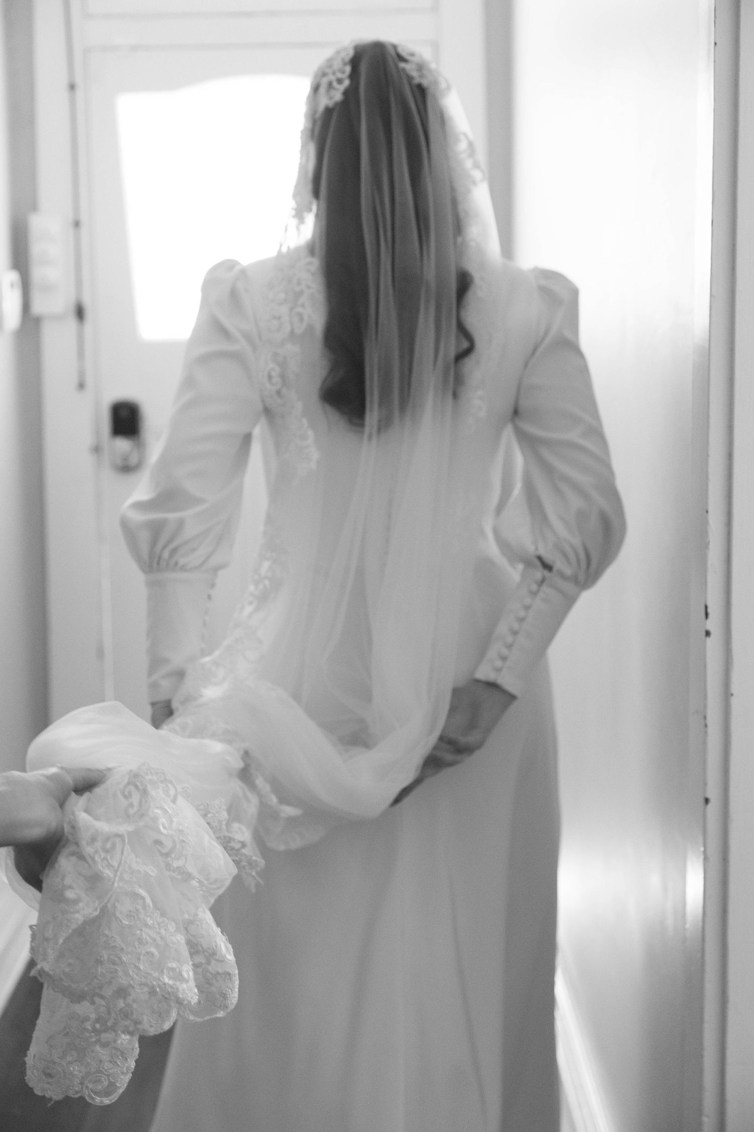 Ethereal black and white portrait of women in flowing white dresses seen from behind in a bright hallway.