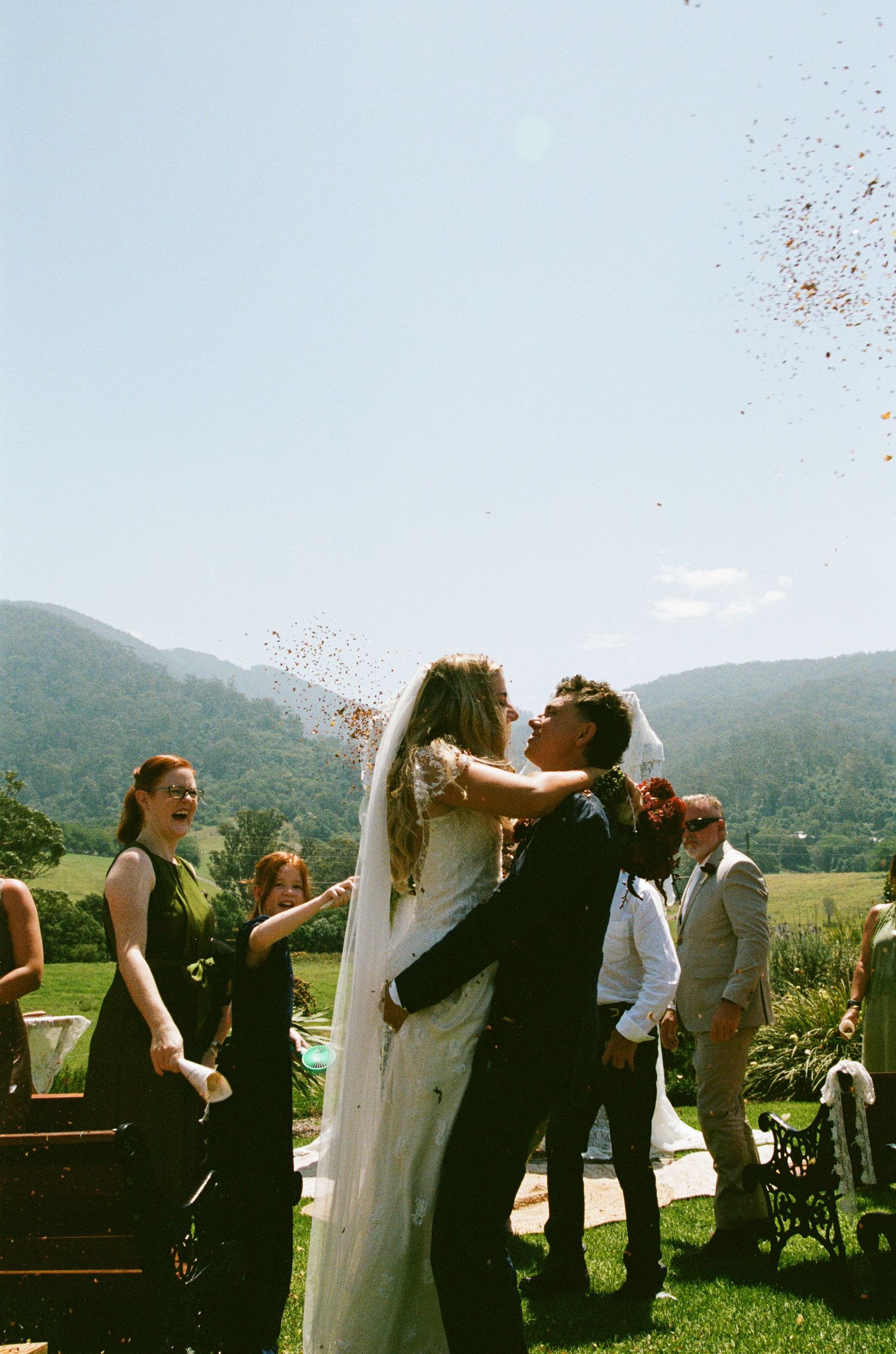 Wedding guests celebrate with the newlyweds on a sunny day with mountains in the background.