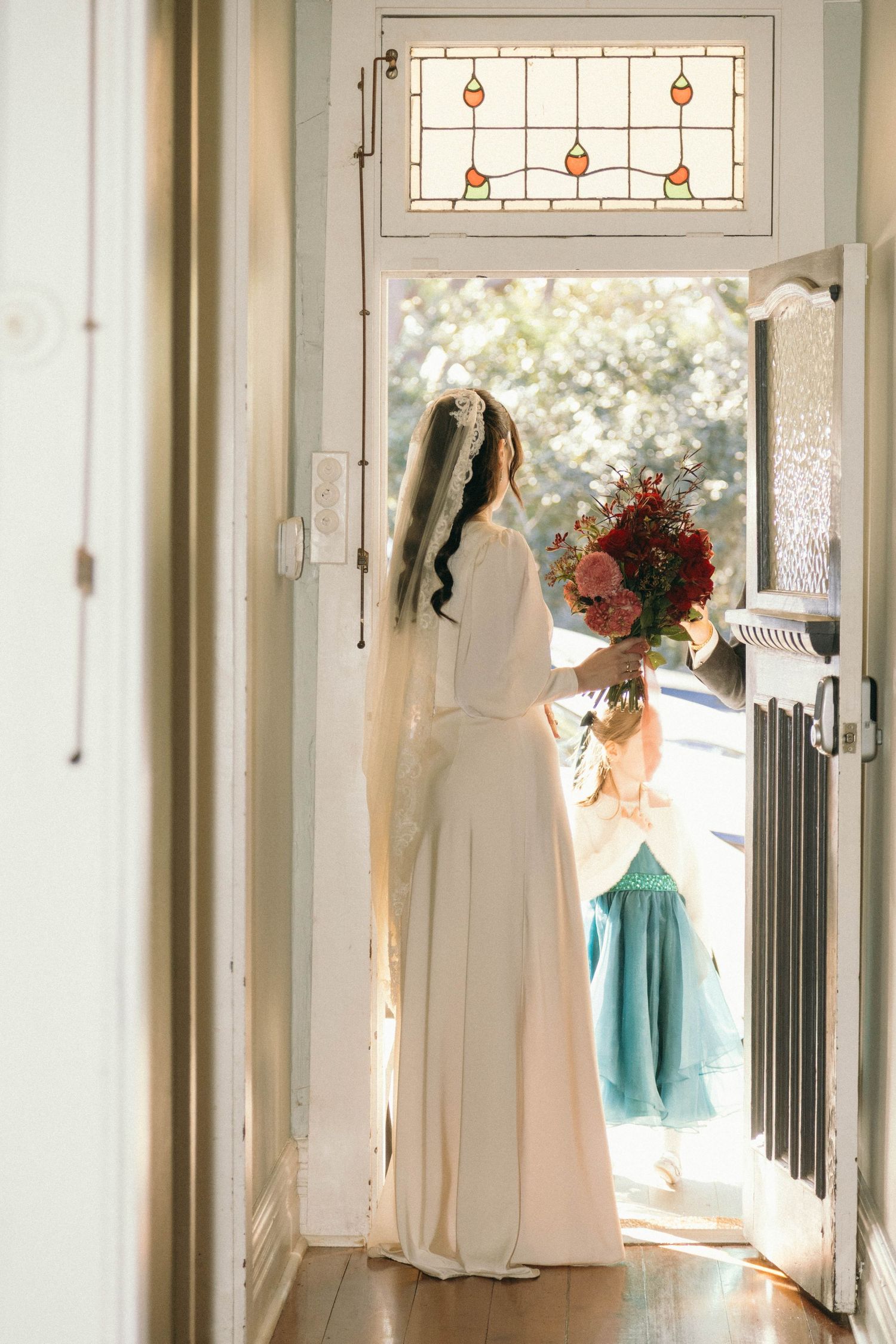 Wedding dresses and bridesmaid gowns in mint green hang elegantly in a bright hallway with stained glass windows.