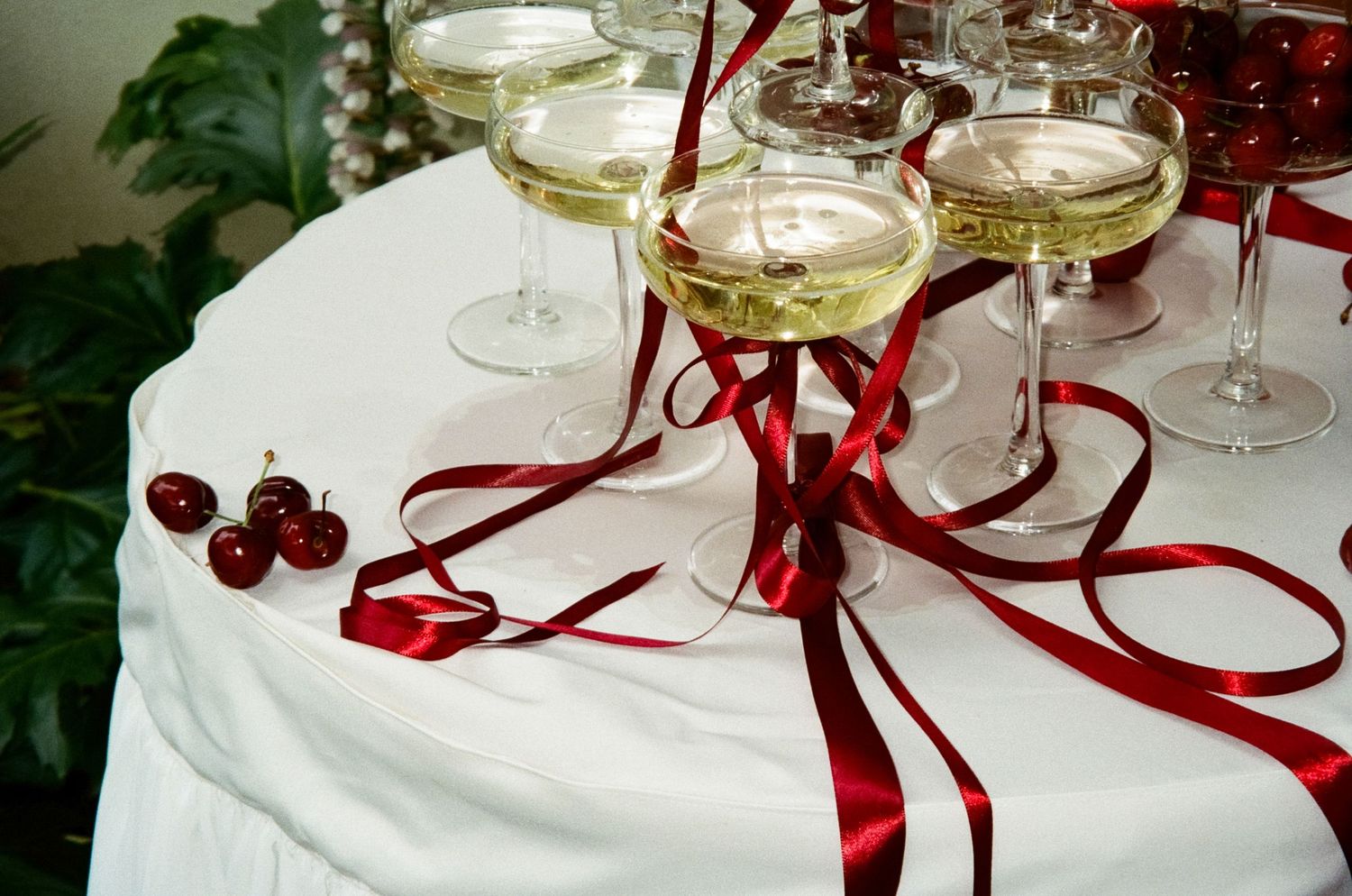 Champagne glasses with red ribbons and fresh cranberries on white tablecloth create an elegant holiday setting.