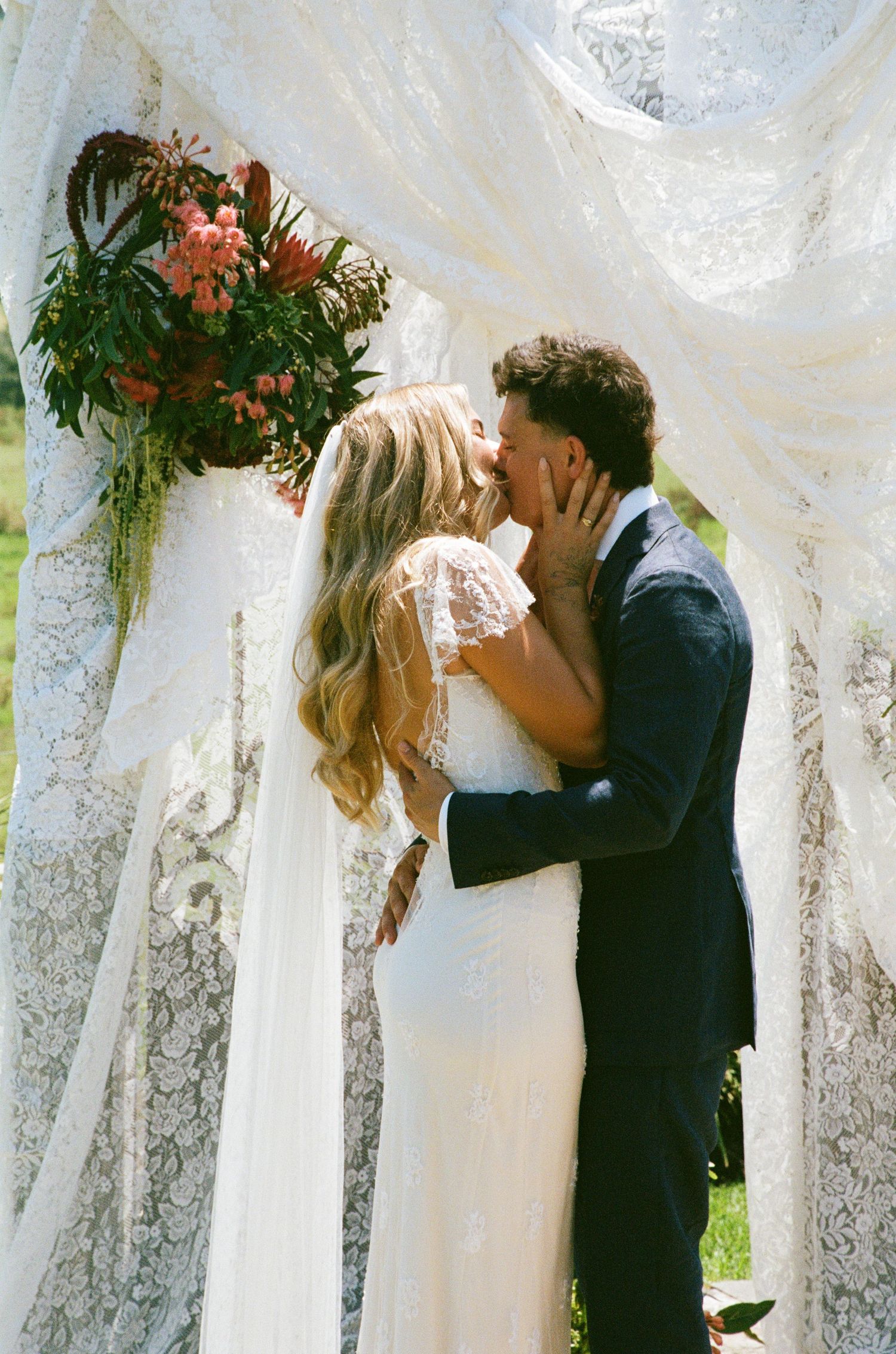 A romantic wedding scene with white lace drapes and hanging floral arrangements.